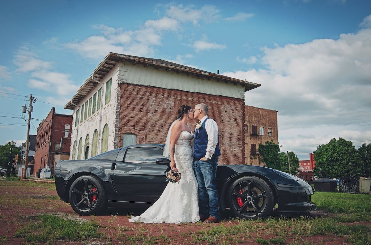 A bride and groom are posing for a picture next to a sports car.