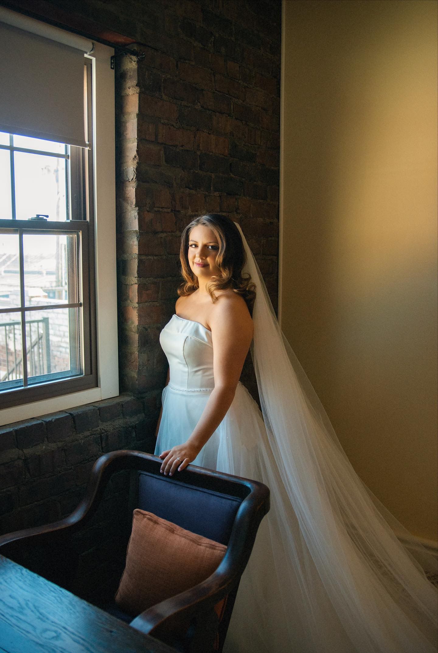 A bride in a wedding dress and veil is standing in front of a window.