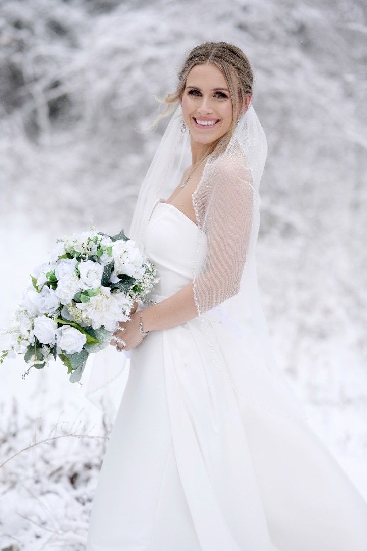 A bride in a wedding dress is holding a bouquet of flowers in the snow.