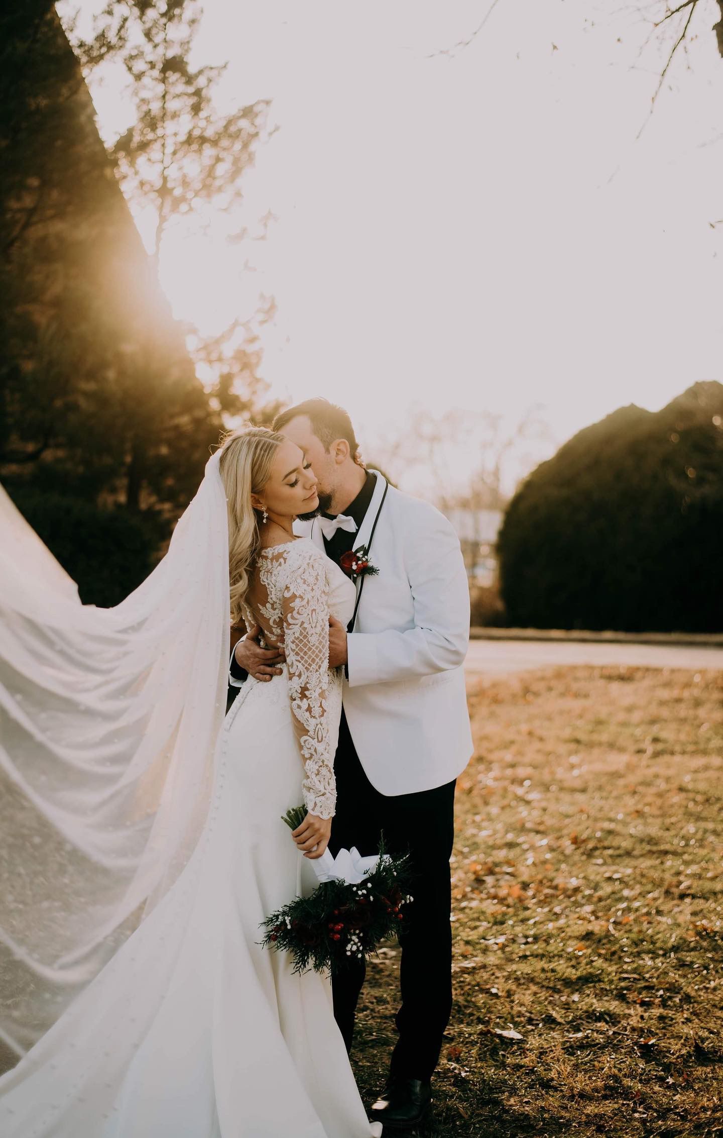 A bride and groom are kissing in a field at their wedding.
