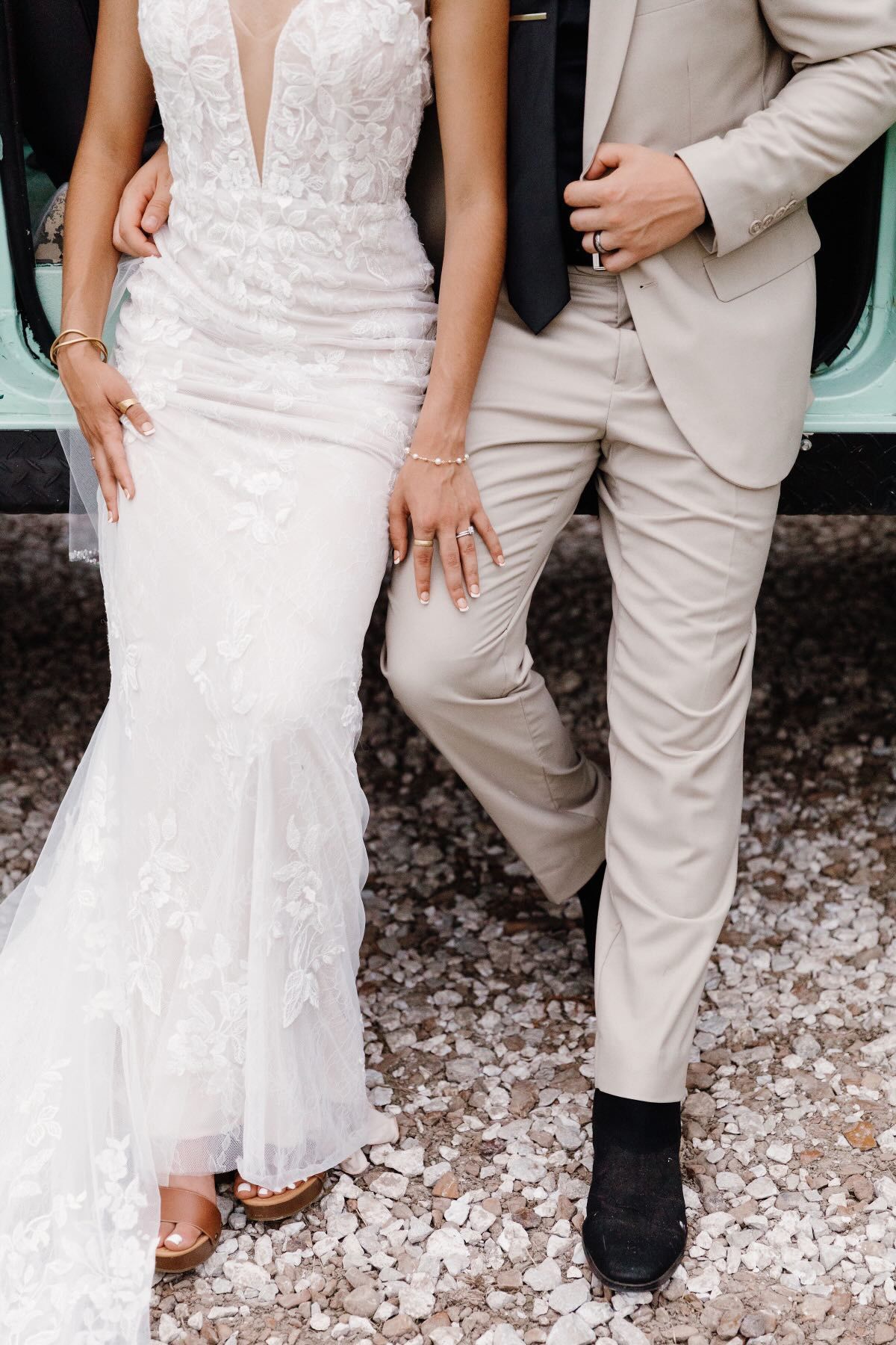A bride and groom are standing next to each other in front of a car.