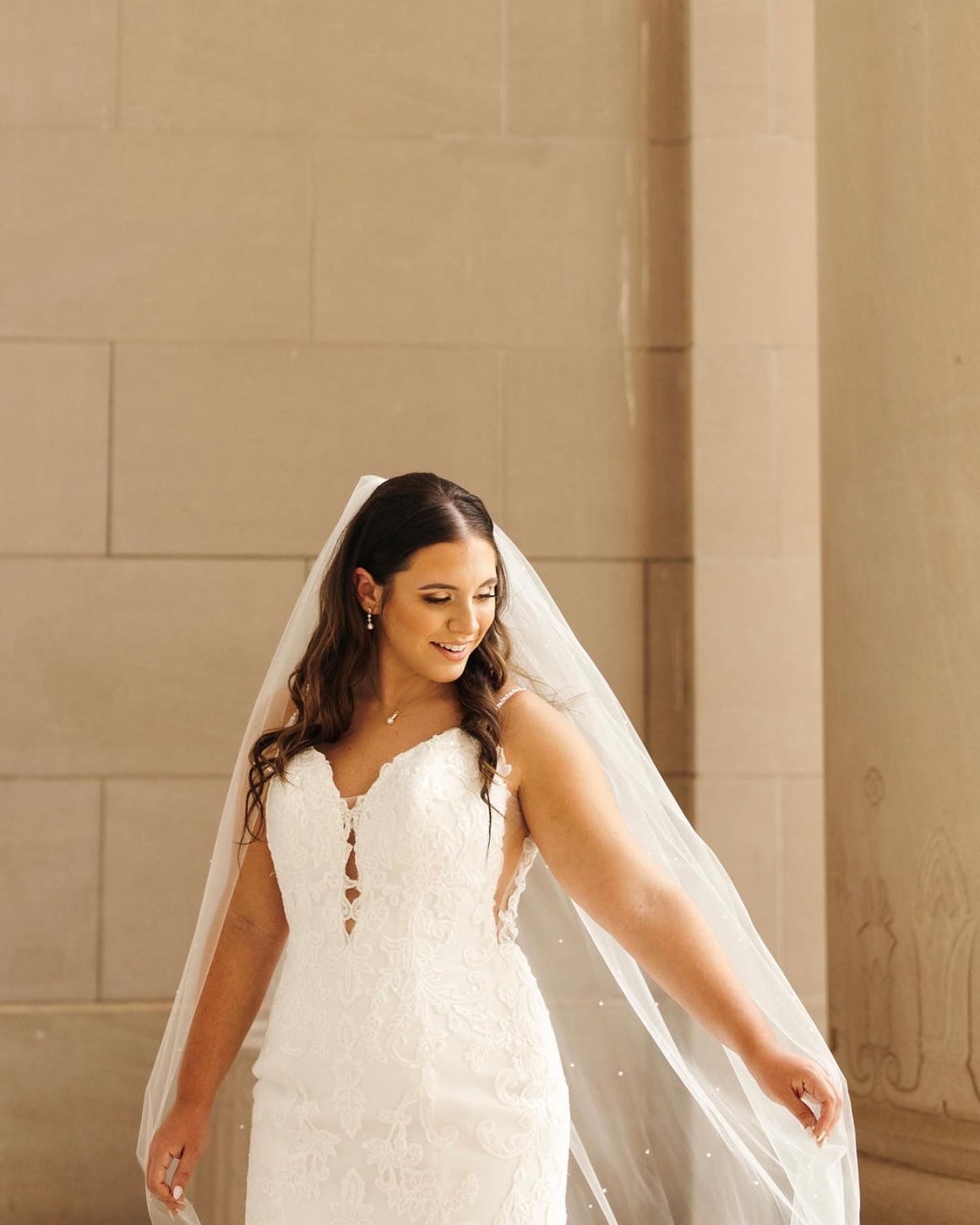 A bride in a white dress and veil is standing in front of a brick wall.