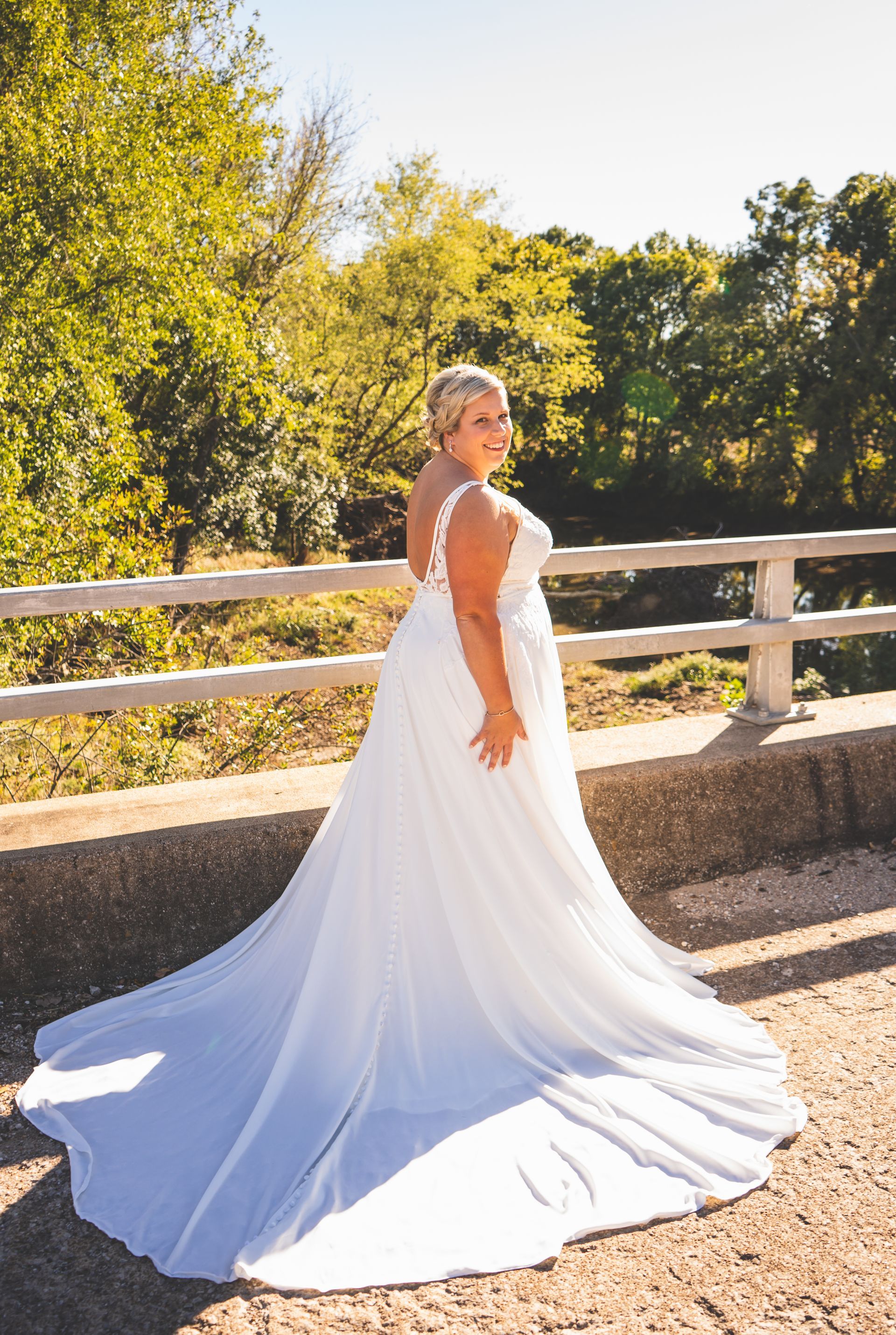 A woman in a white wedding dress is standing on a bridge.