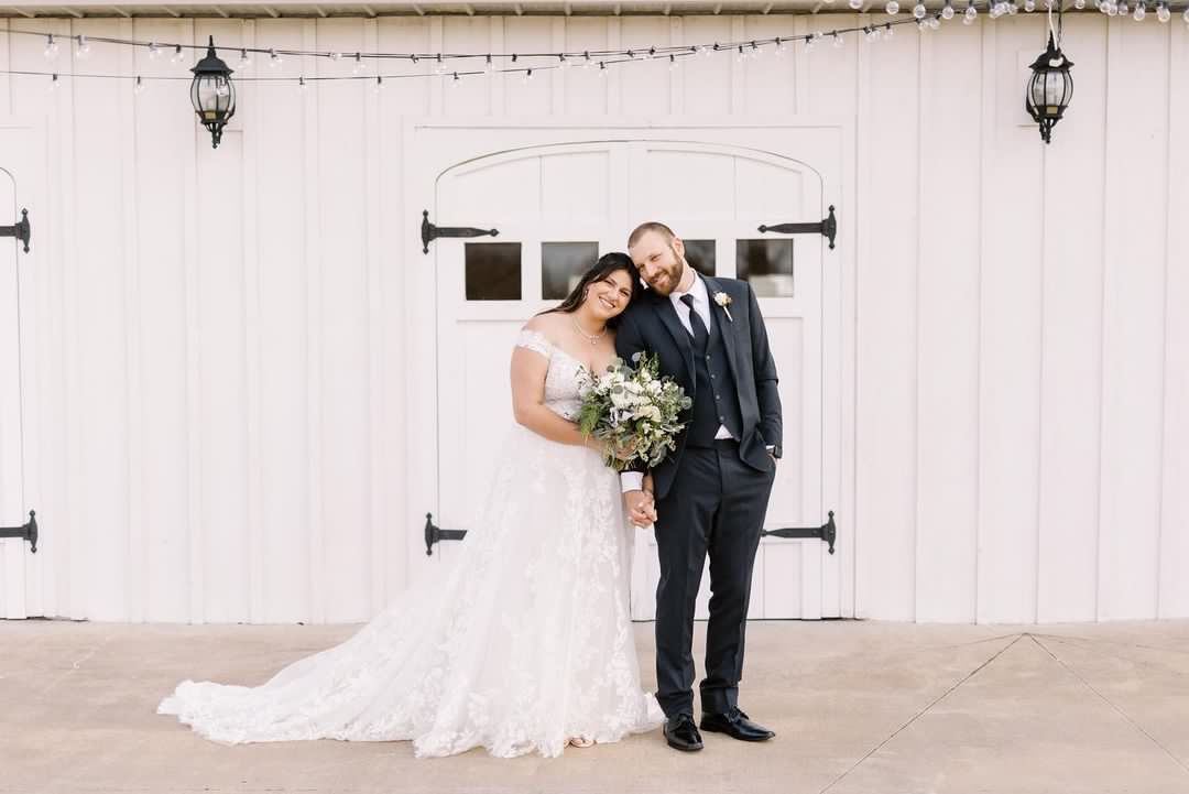A bride and groom are posing for a picture in front of a white barn.