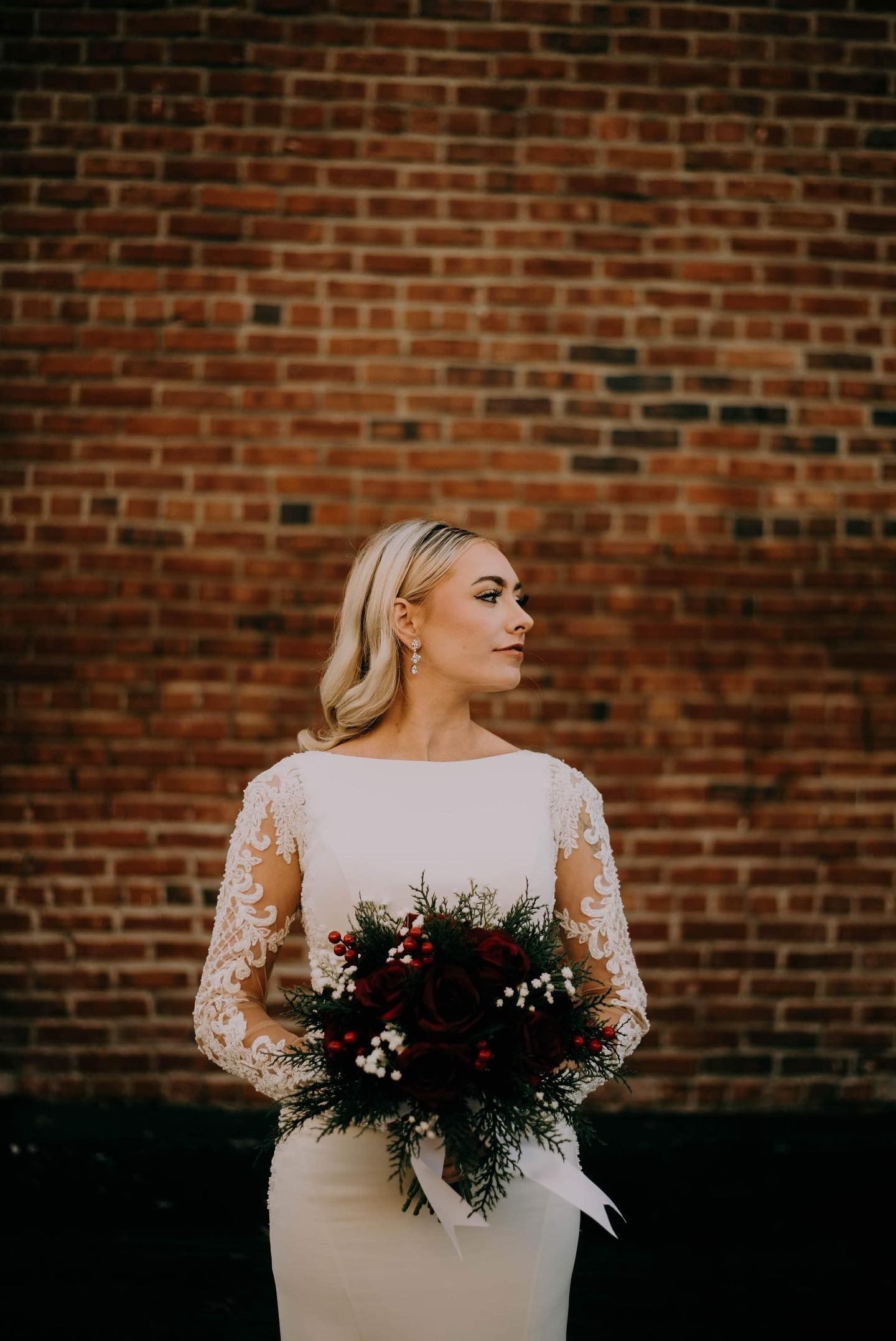 A bride in a white dress is holding a bouquet of flowers in front of a brick wall.