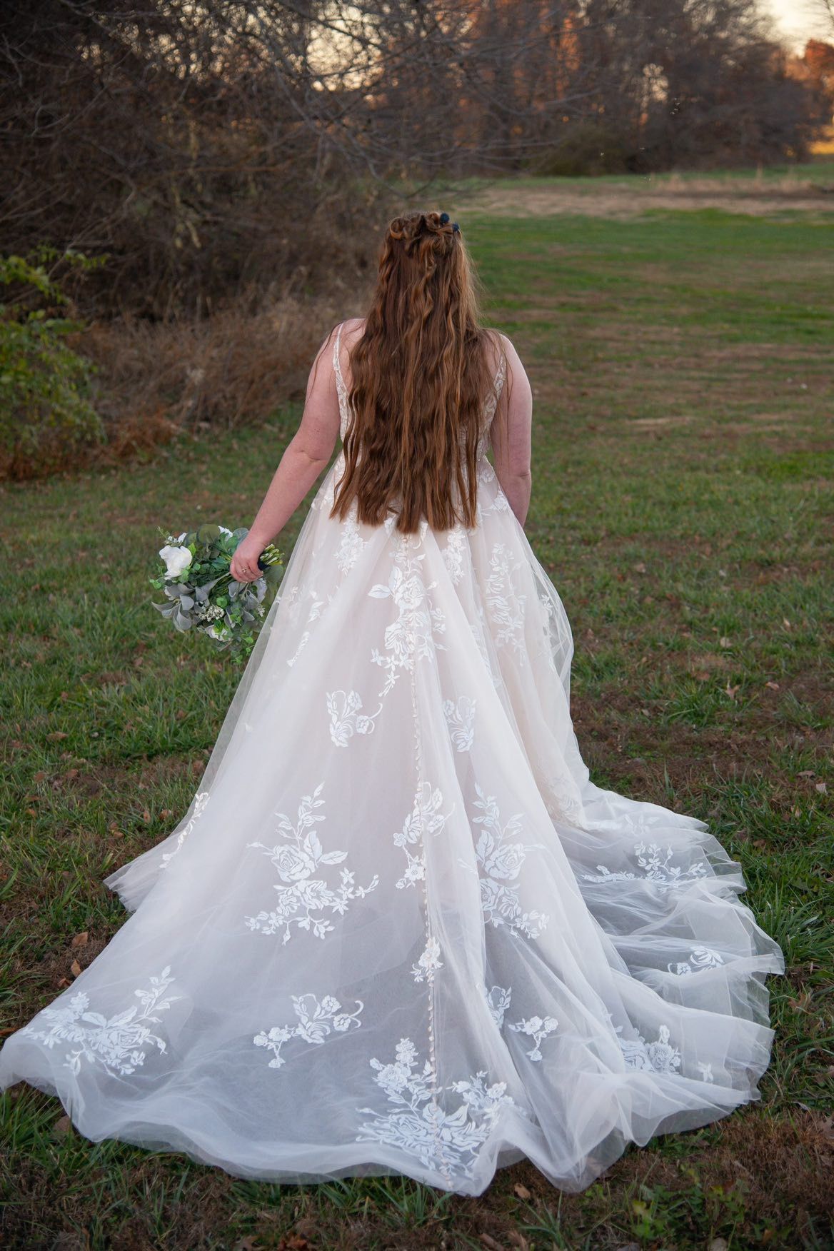 A woman in a wedding dress is standing in a field holding a bouquet of flowers.