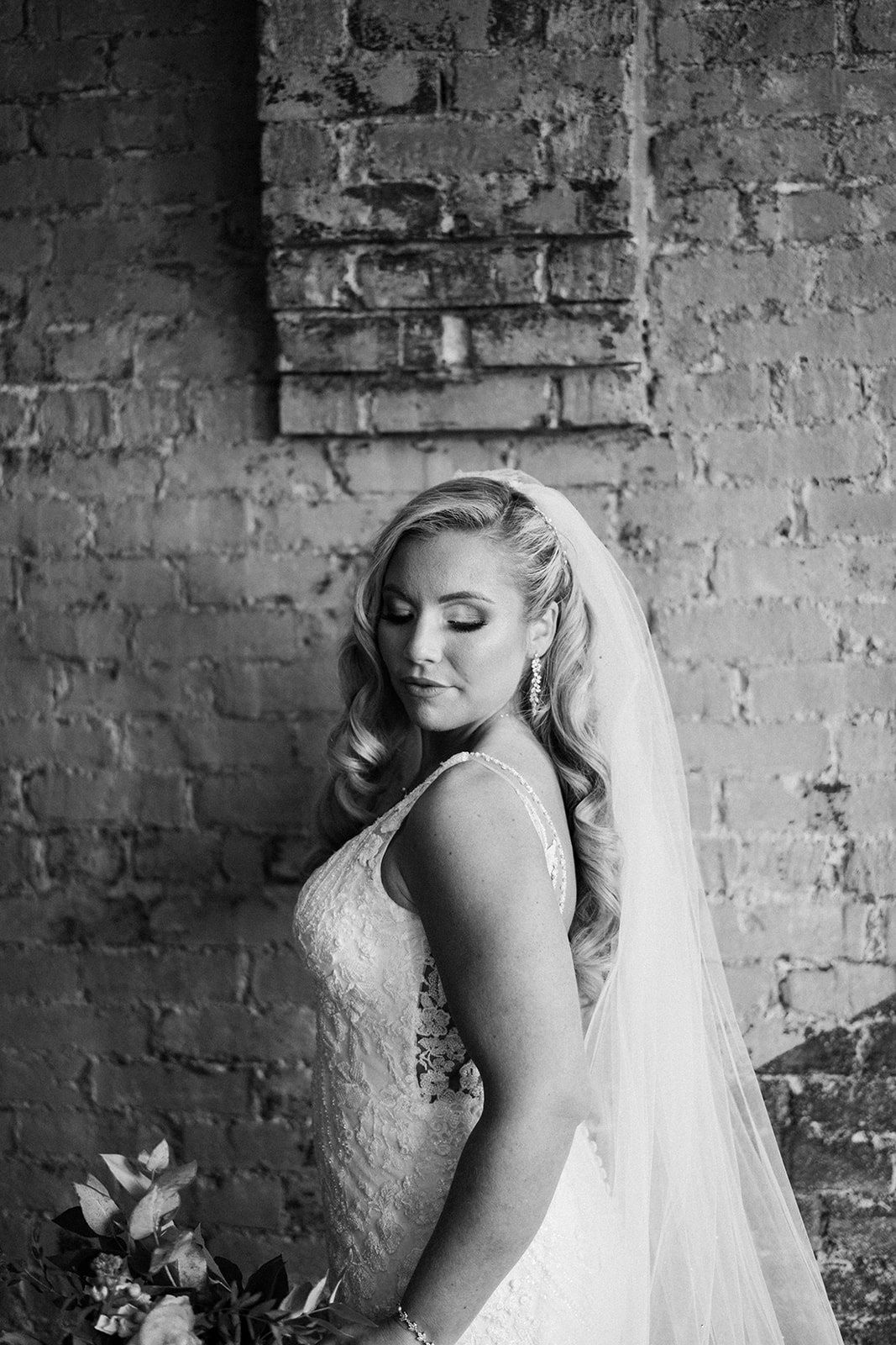 A bride in a wedding dress and veil is standing in front of a brick wall.