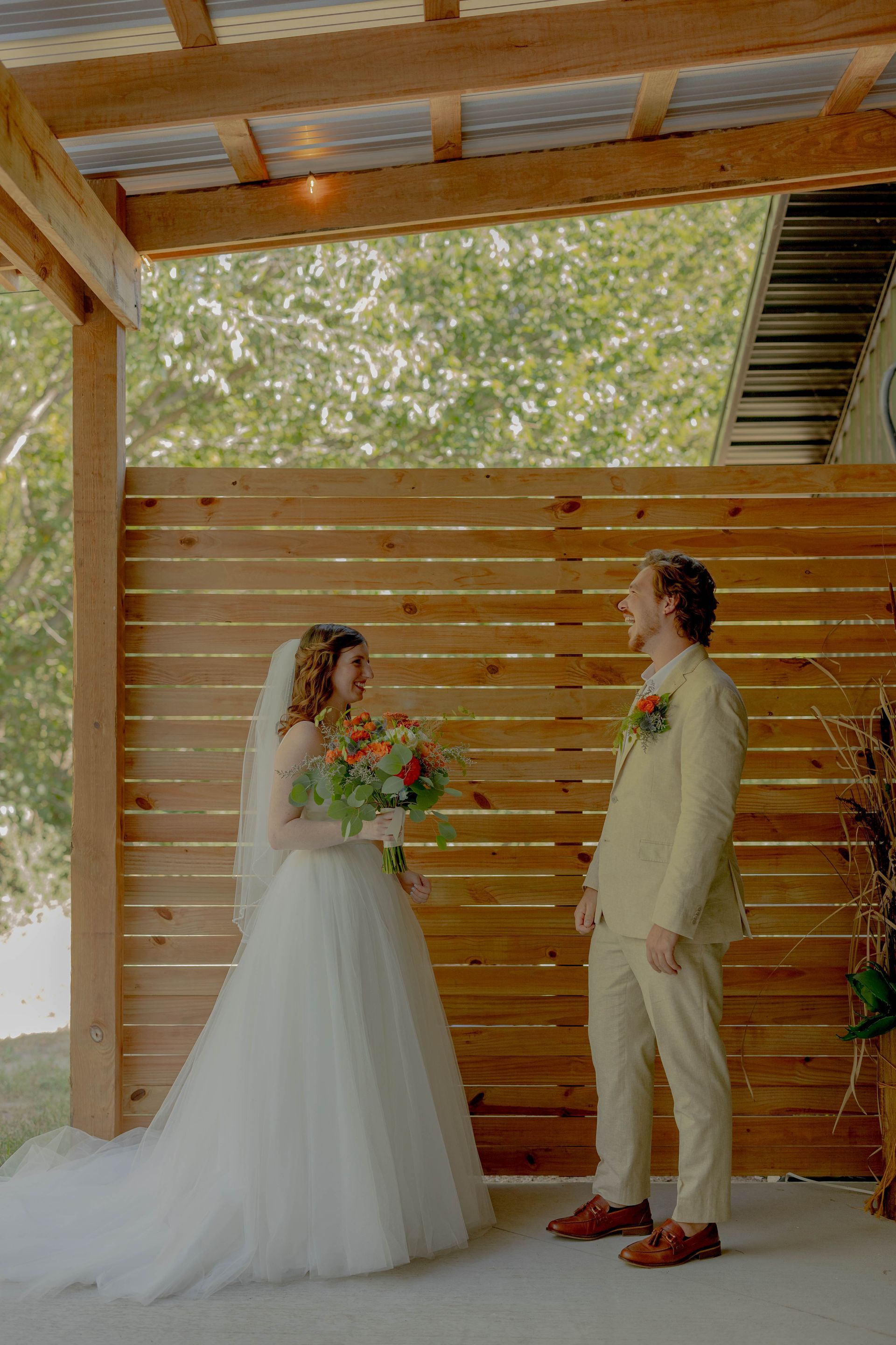 A bride and groom are standing in front of a wooden fence.