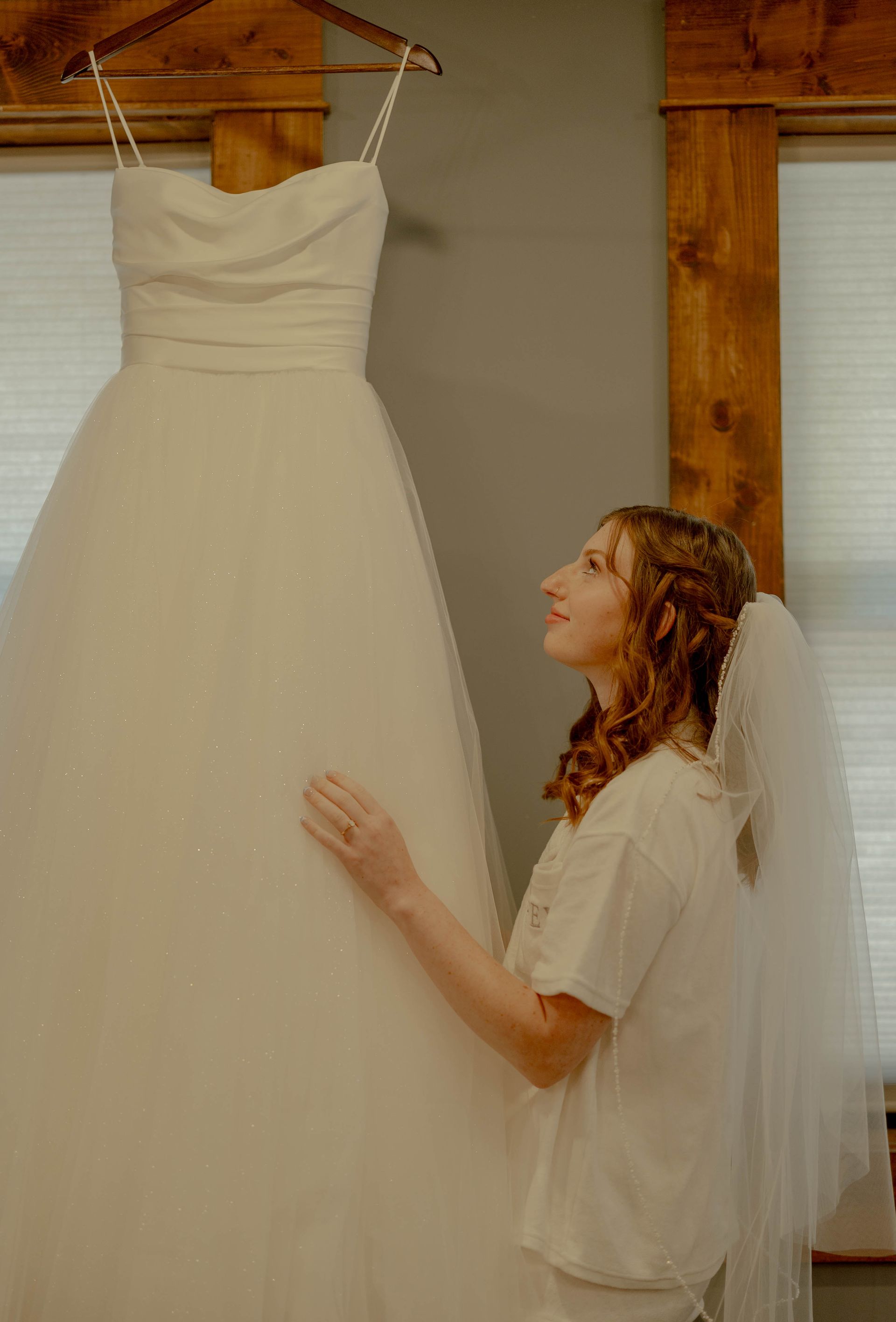 A bride is looking at her wedding dress hanging on a hanger.