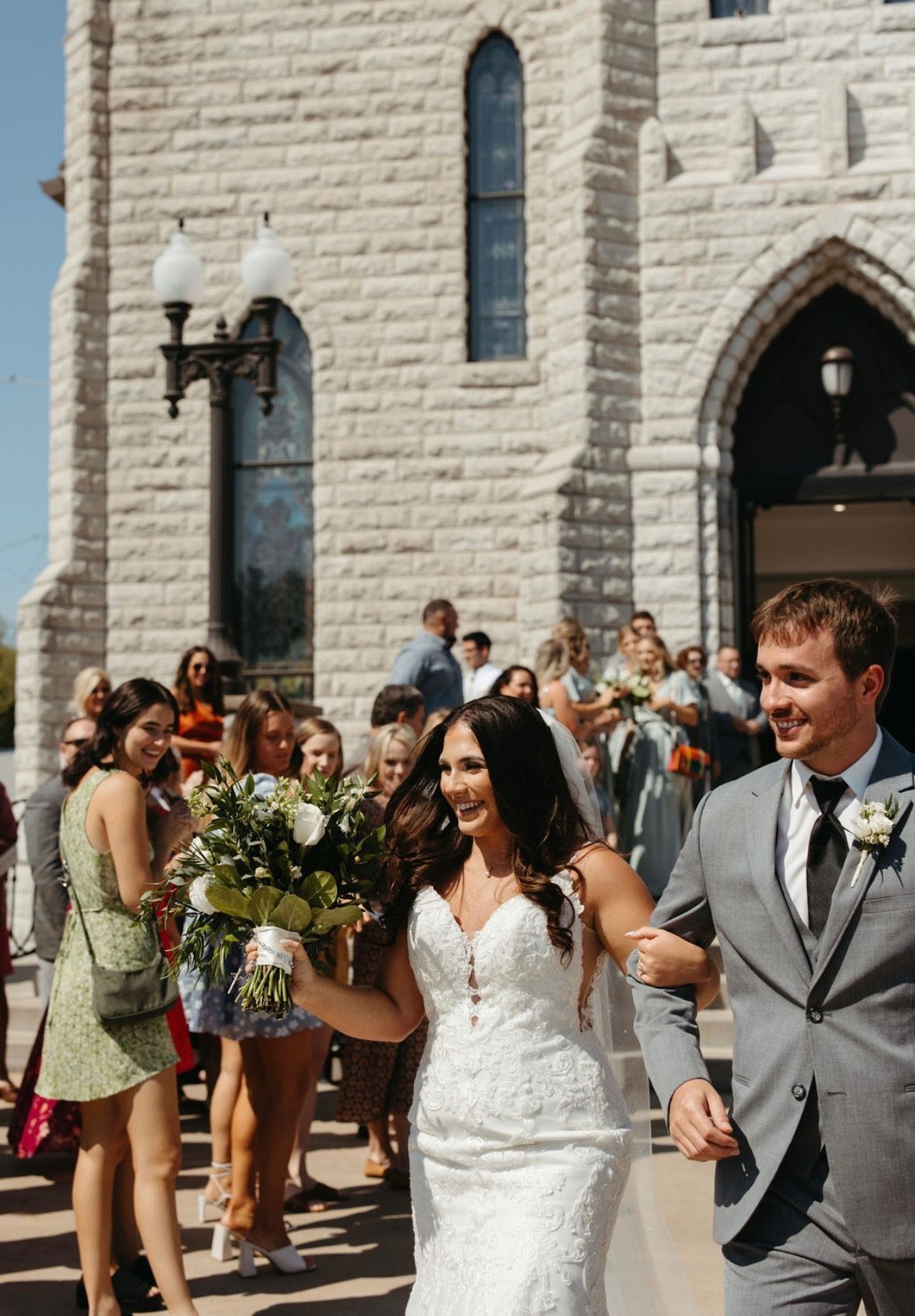 A bride and groom are walking out of a church holding hands.