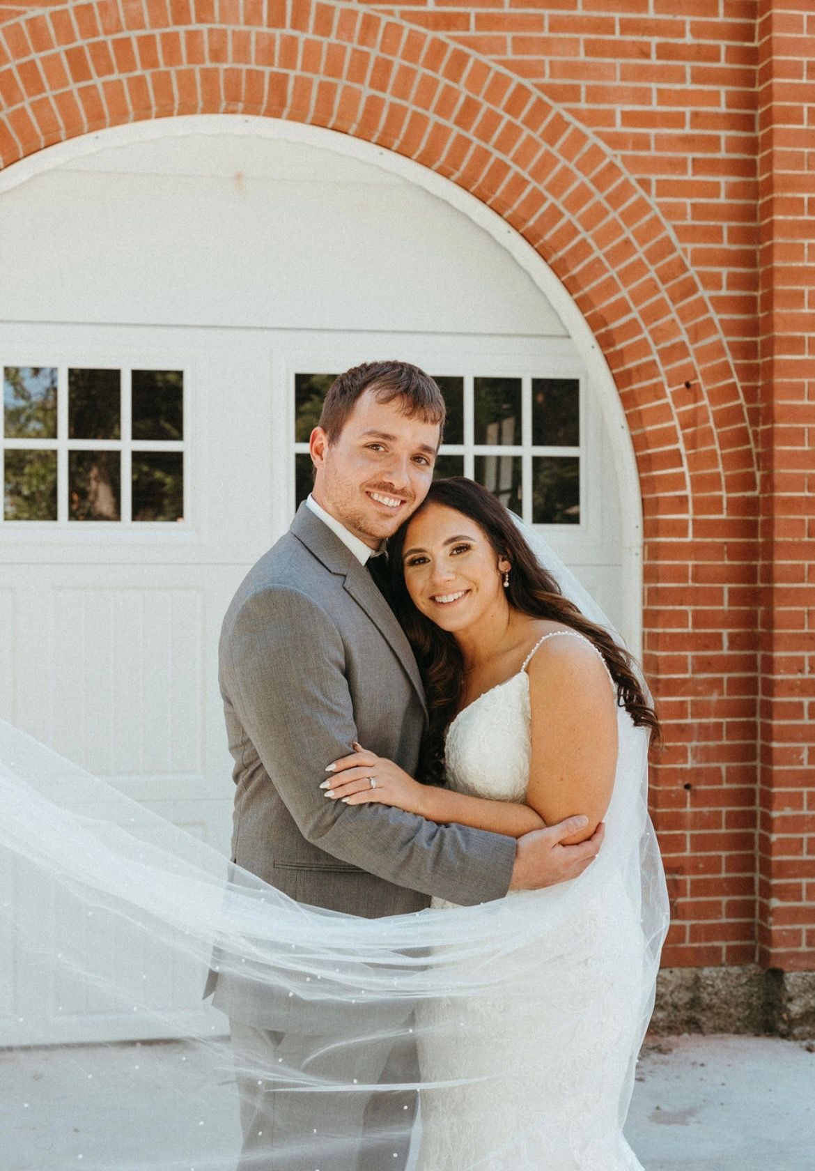 A bride and groom are posing for a picture in front of a brick building.