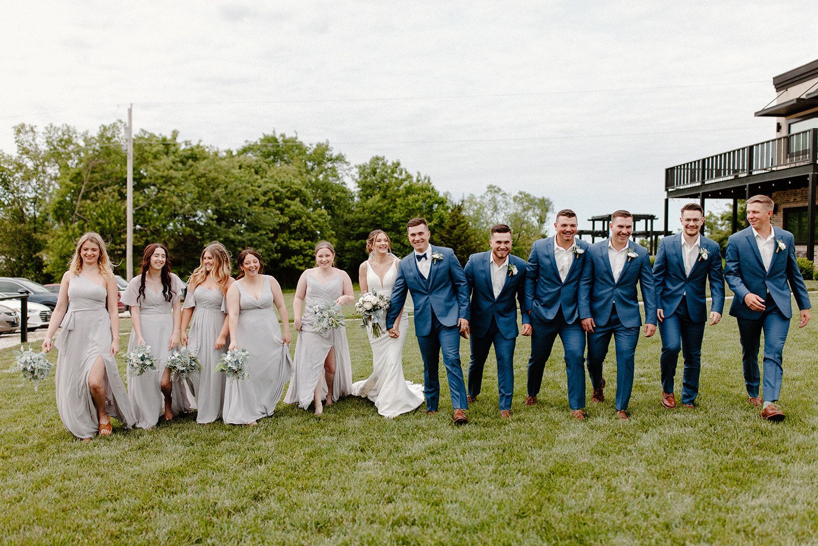 A bride and groom are walking with their wedding party in a field.