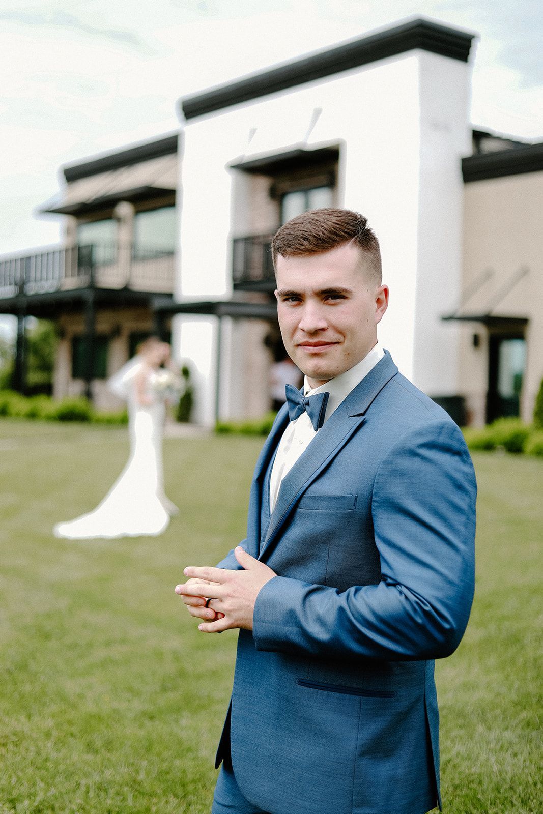 The groom is wearing a blue suit and bow tie and the bride is wearing a white dress.