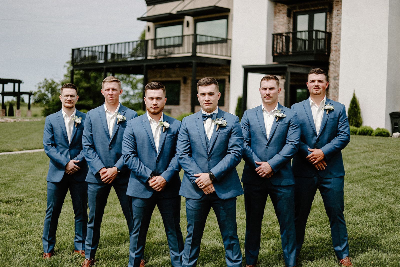 The groom and his groomsmen are posing for a picture in front of a house.