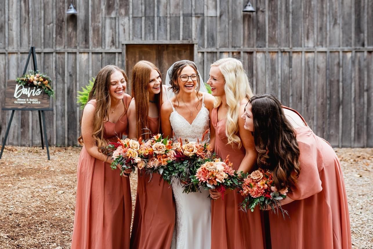 A bride and her bridesmaids are posing for a picture in front of a barn.