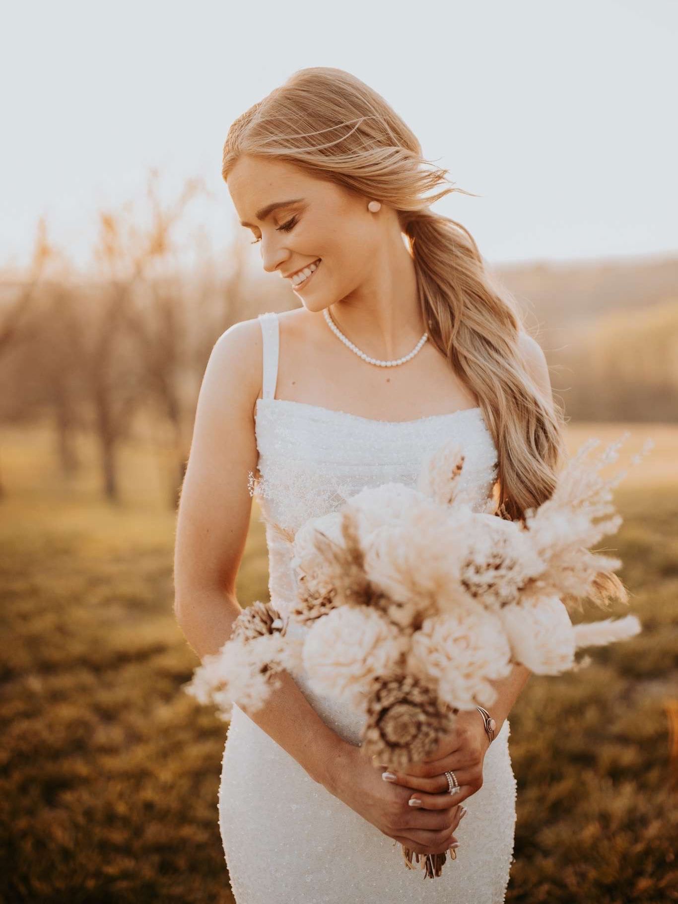 A woman in a wedding dress with a high slit is standing in front of palm trees.