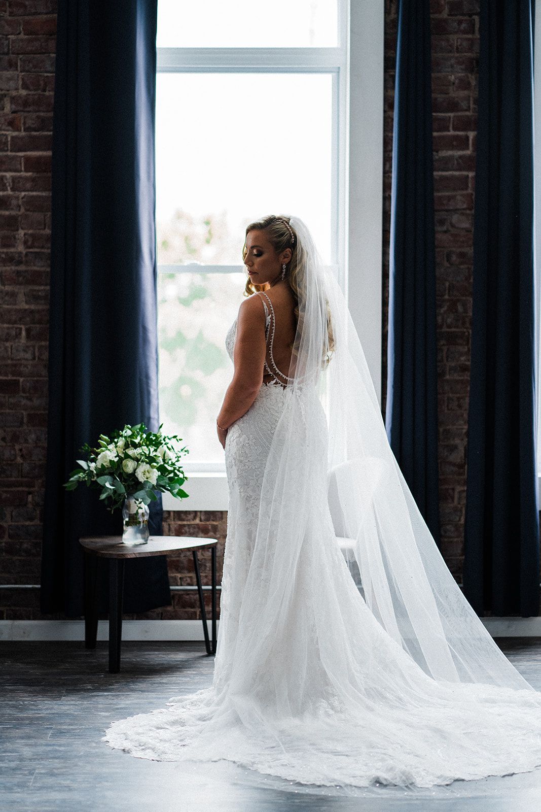 A bride in a wedding dress and veil is standing in front of a window.