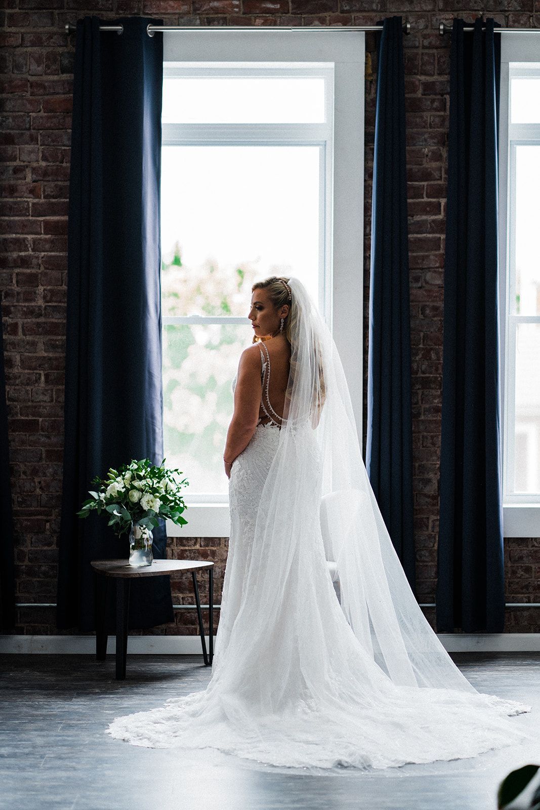 A bride in a wedding dress and veil is standing in front of a window.