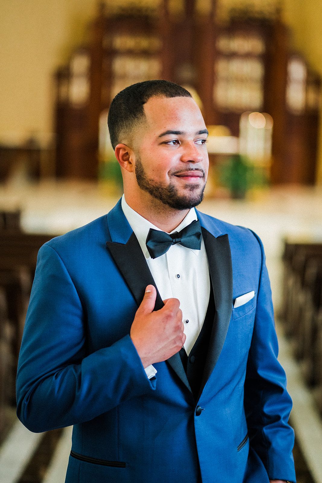 A man in a blue tuxedo and bow tie is standing in a church.
