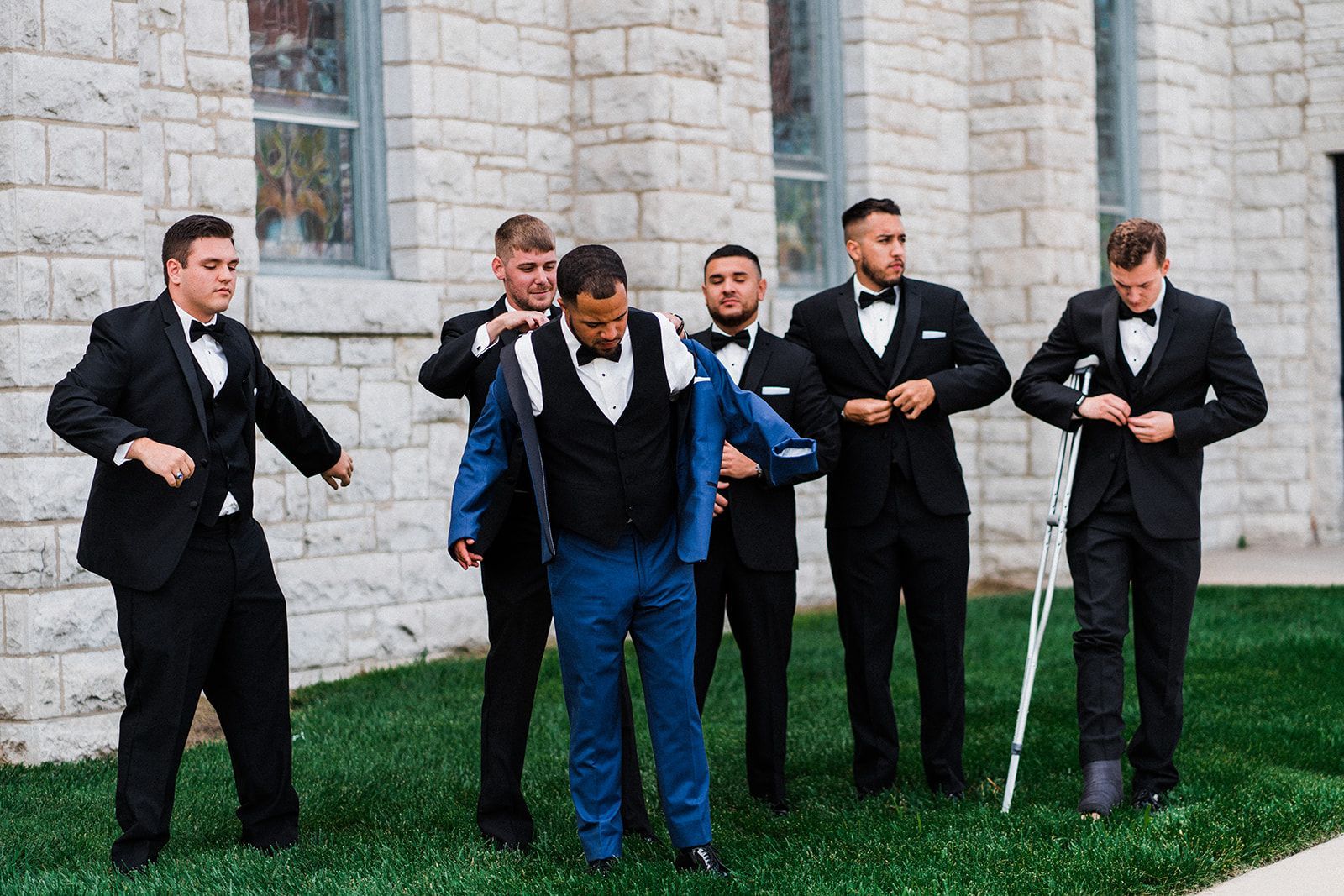 A group of men in suits and bow ties are standing in front of a brick building.