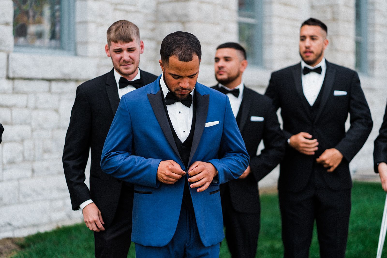A man in a blue tuxedo is standing next to his groomsmen.