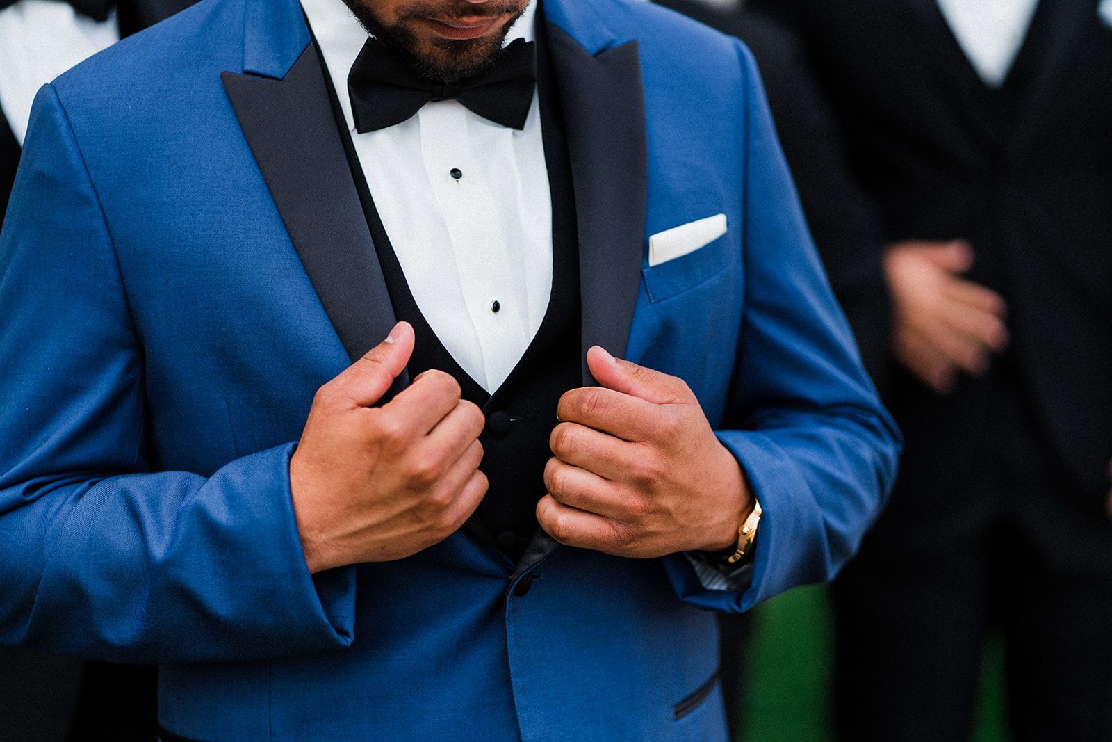 A man in a blue tuxedo and bow tie is adjusting his jacket.