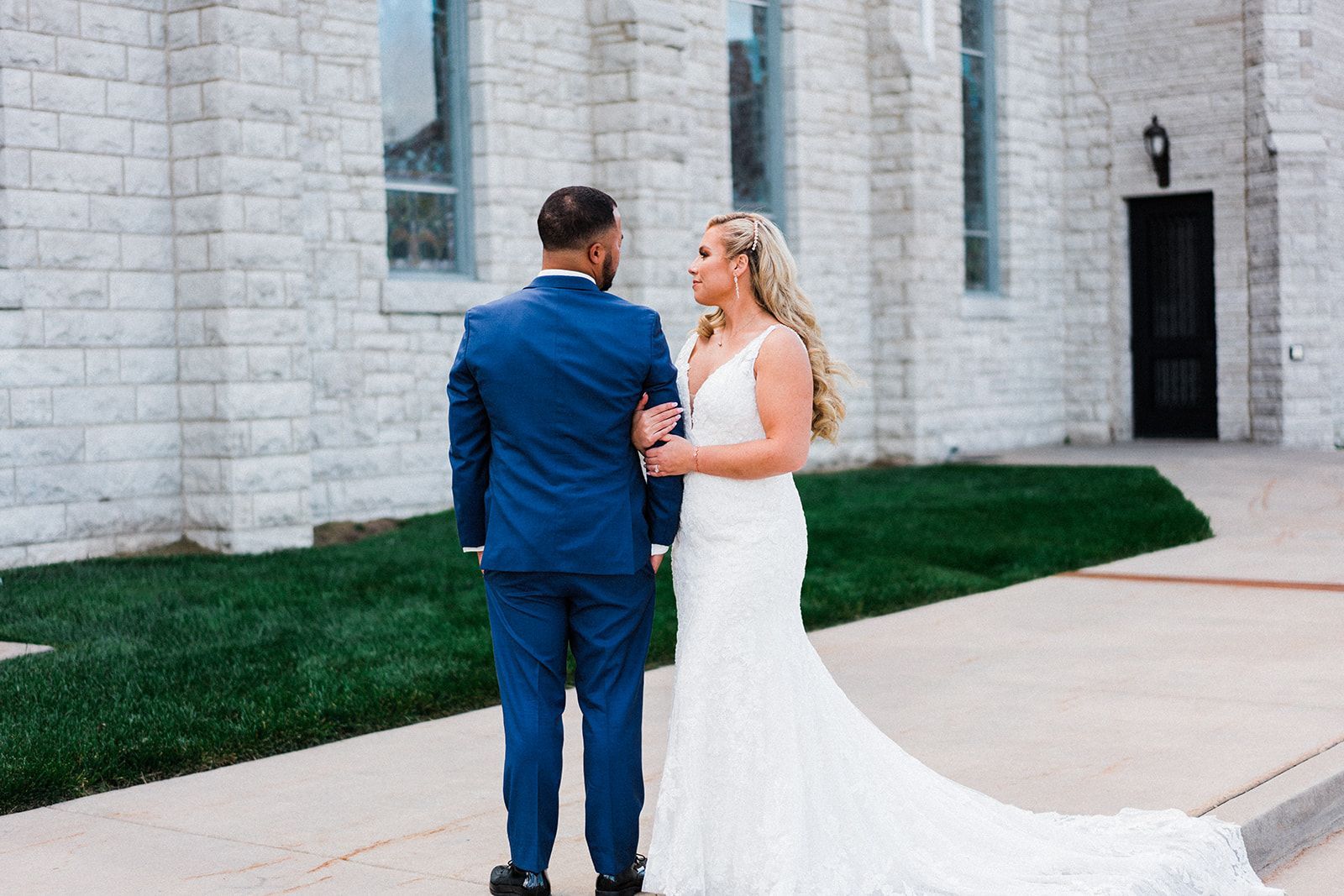 A bride and groom are standing in front of a church holding hands.