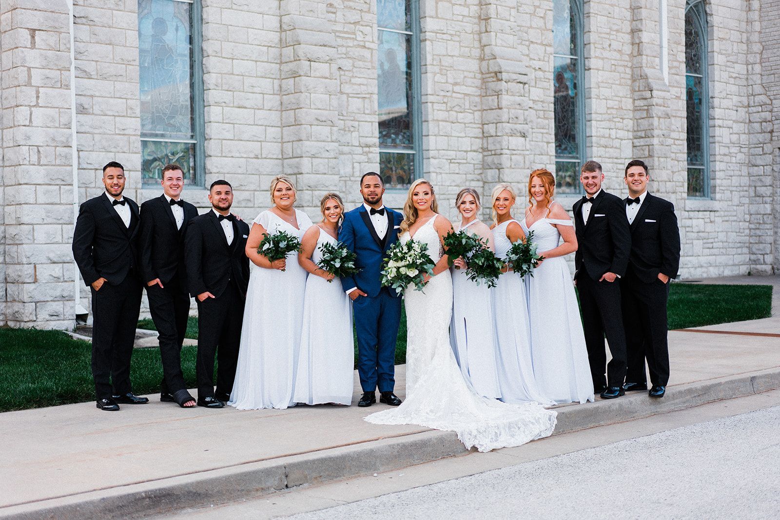 The bride and groom are posing for a picture with their wedding party in front of a church.