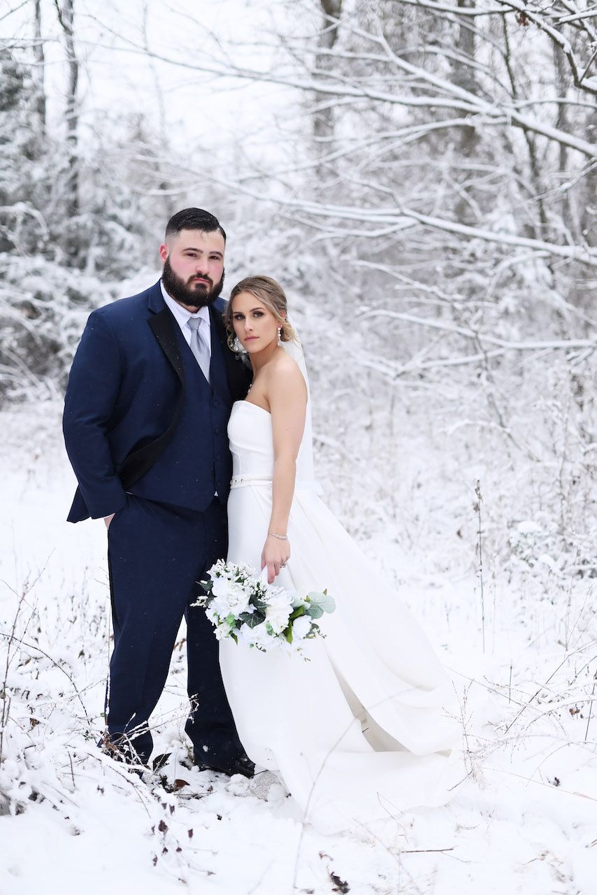 A bride and groom are posing for a picture in the snow.