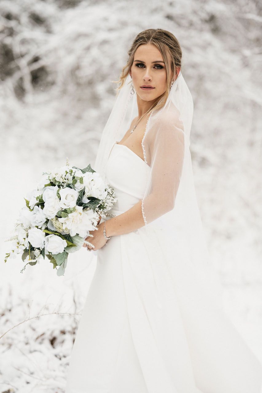 A bride in a white dress is holding a bouquet of flowers in the snow.