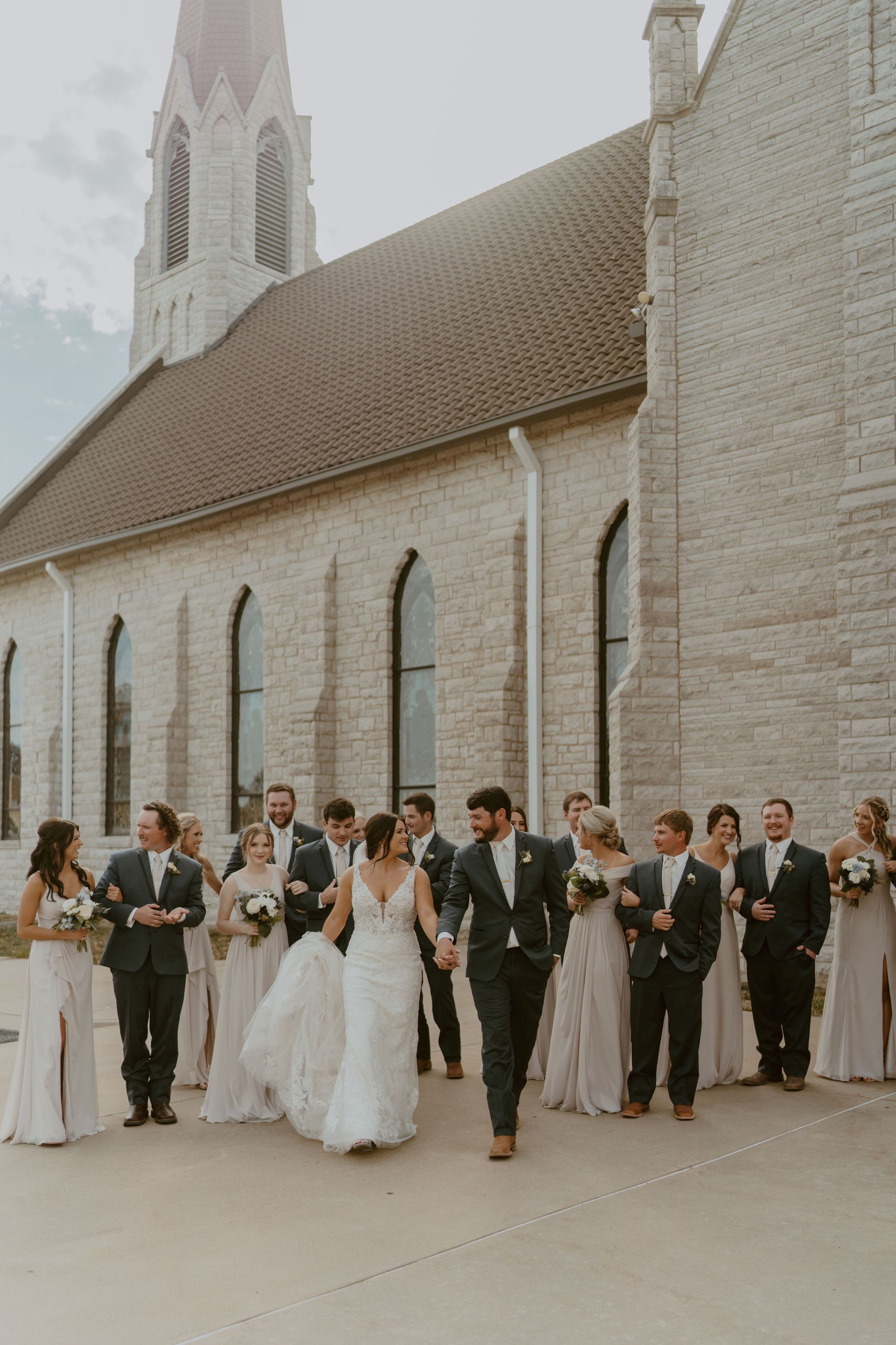 A bride and groom are walking with their wedding party in front of a church.