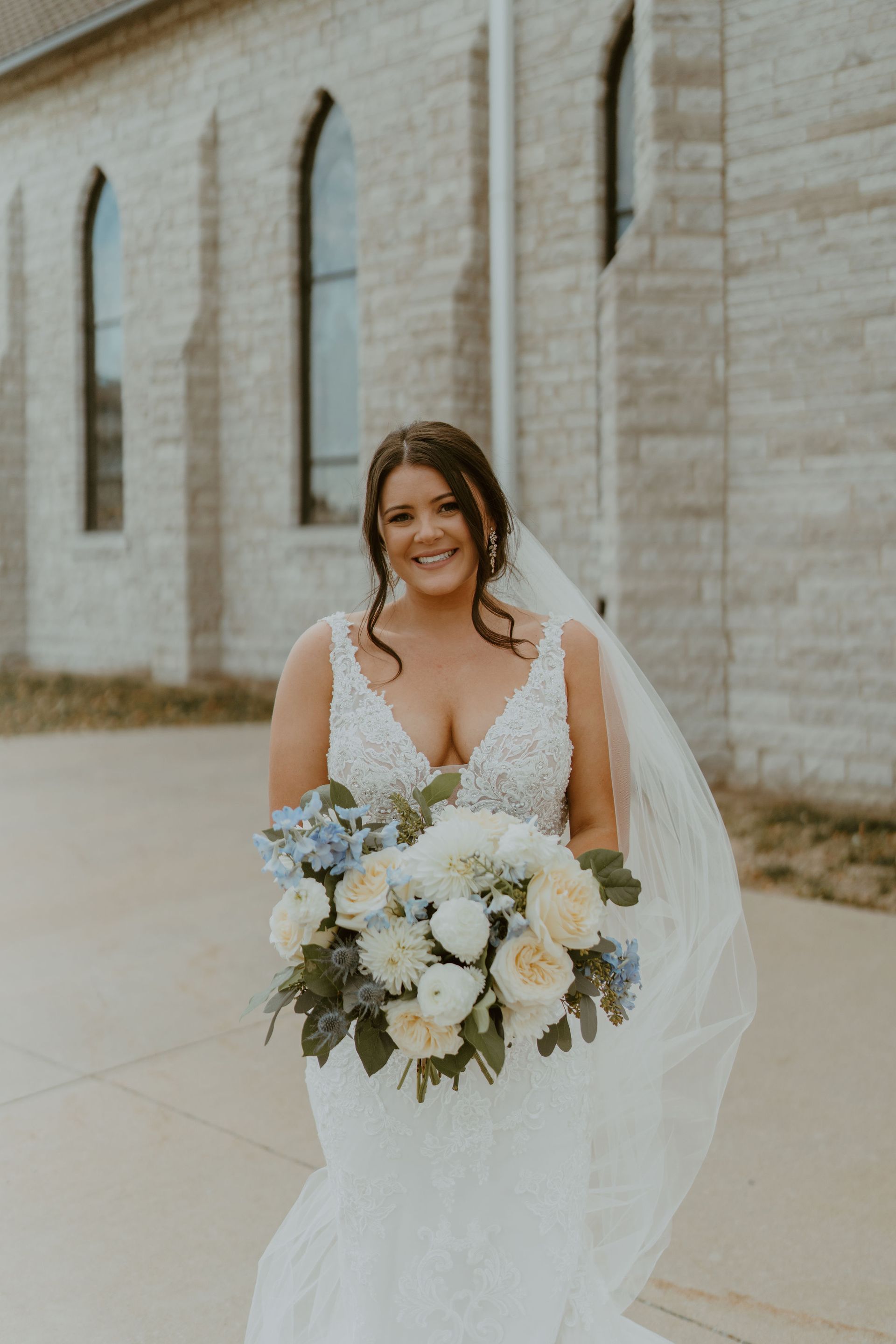 A bride in a wedding dress and veil is holding a bouquet of flowers in front of a church.