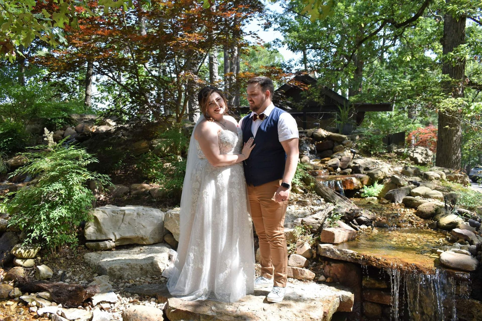 A bride and groom are posing for a picture in front of a waterfall.