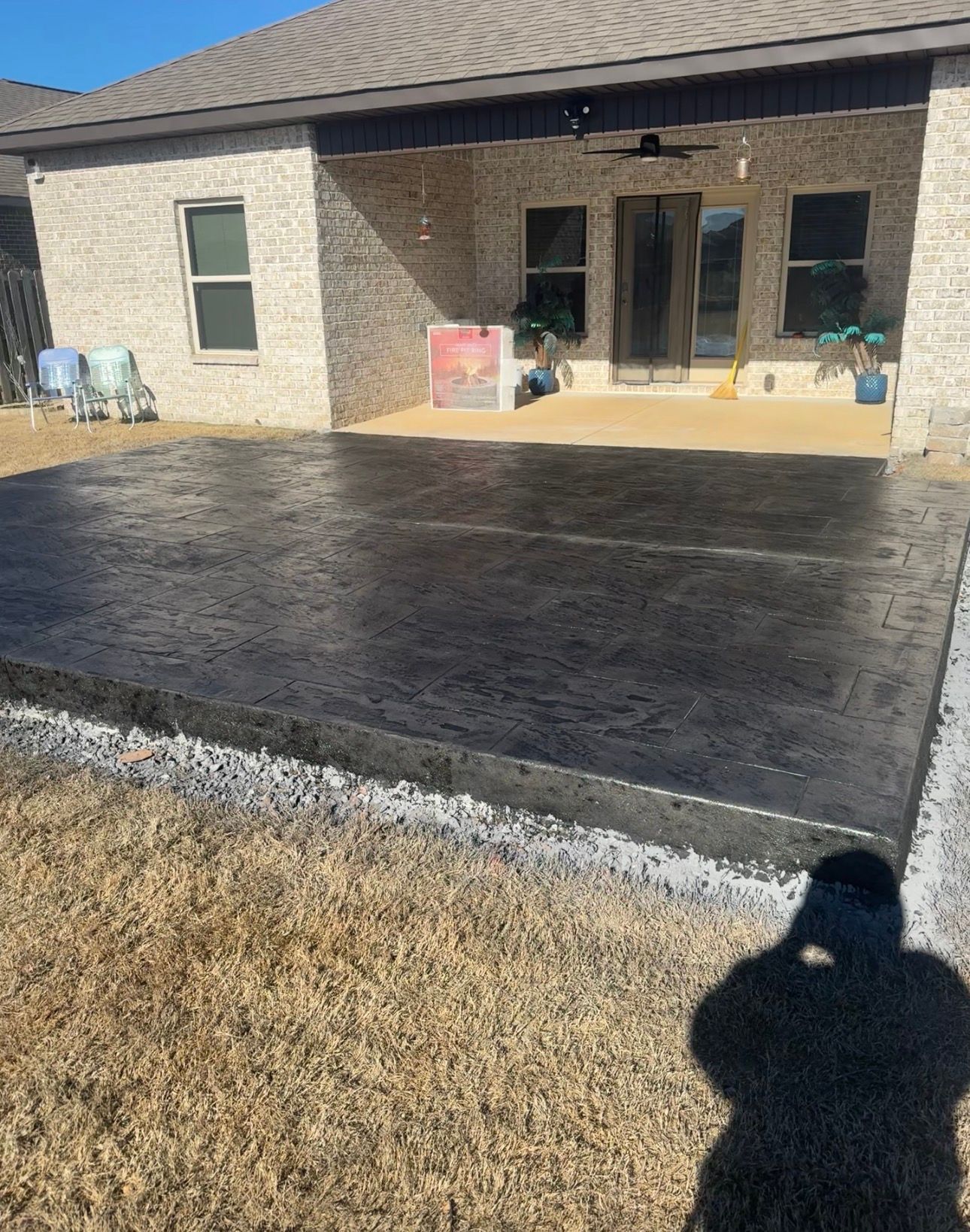 Freshly poured dark concrete patio in front of a brick house with a covered porch and doors.