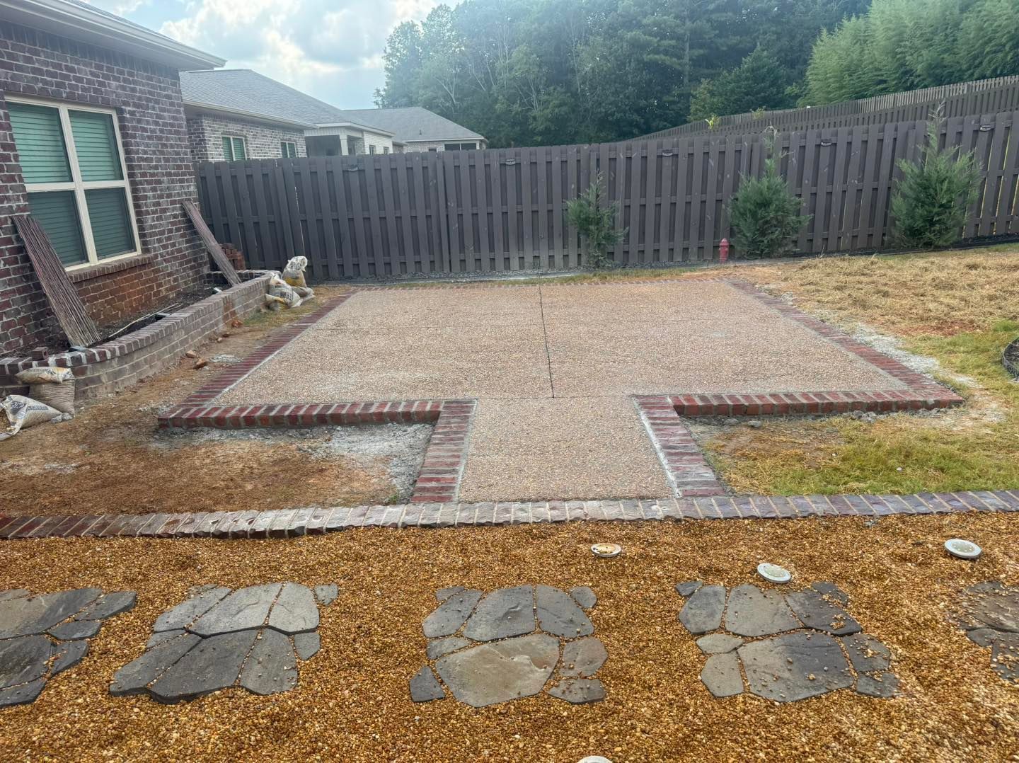 Backyard patio with a brick and paver platform, low retaining walls, and a wooden fence behind.
