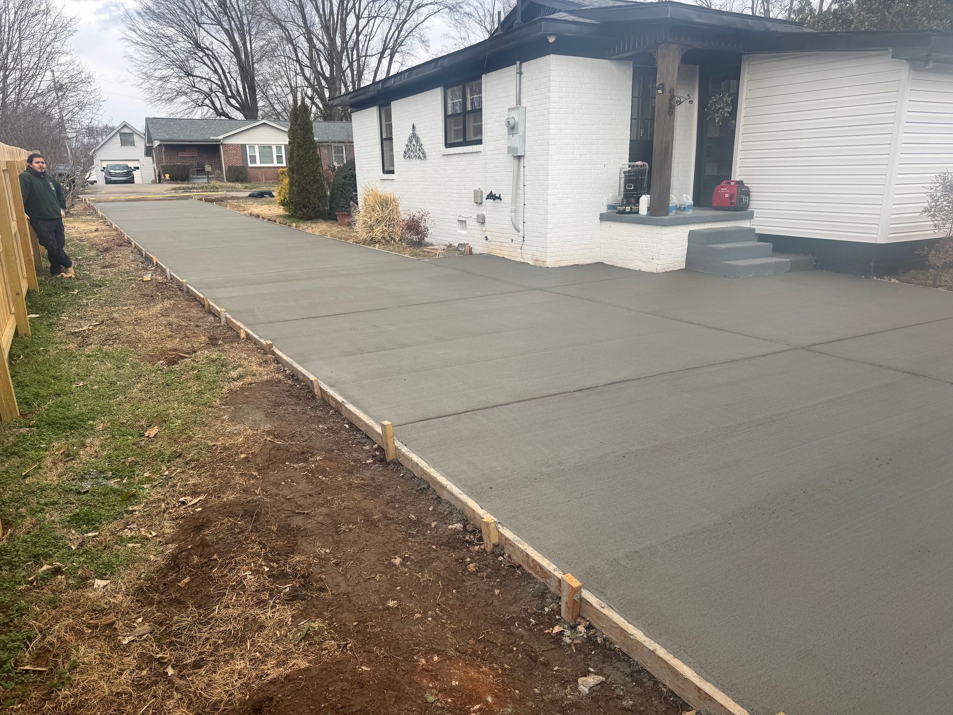 Freshly poured concrete driveway beside a white house in a residential yard