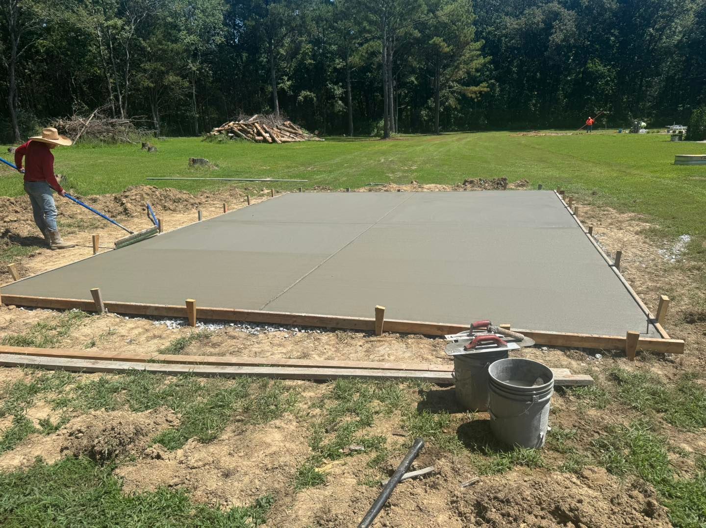 Fresh concrete slab being poured at an outdoor construction site, with workers and buckets nearby