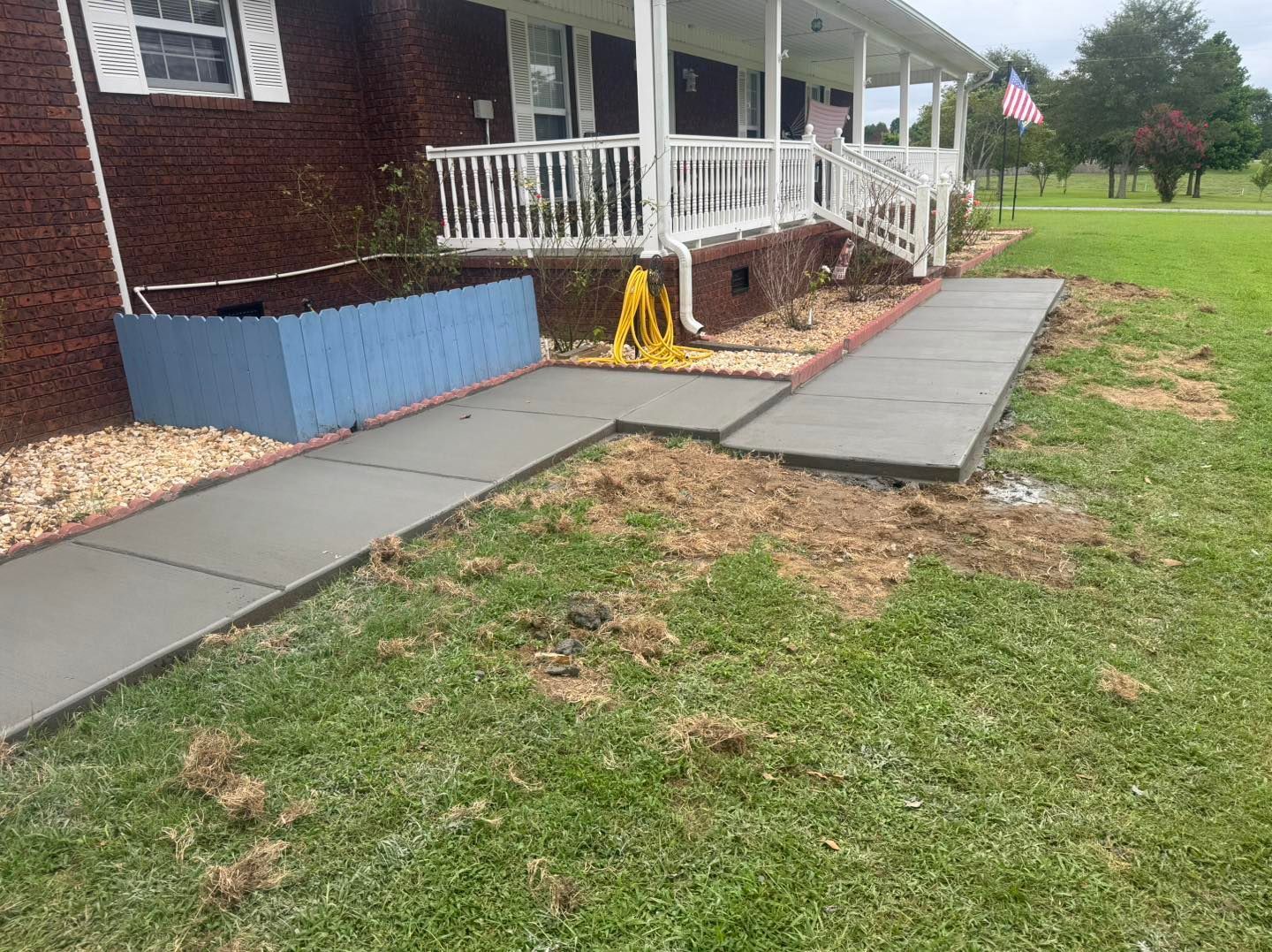 Concrete walkway beside a porch ramp with white railings and a yellow caution sign, leading over grass.