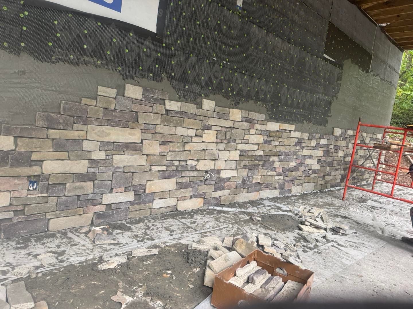 Snowy construction site with stone wall, red scaffolding, and debris on the ground