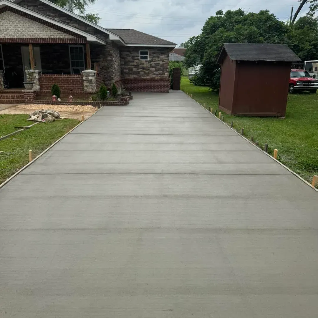 Fresh concrete driveway leading to a brick house with a small shed and green lawn