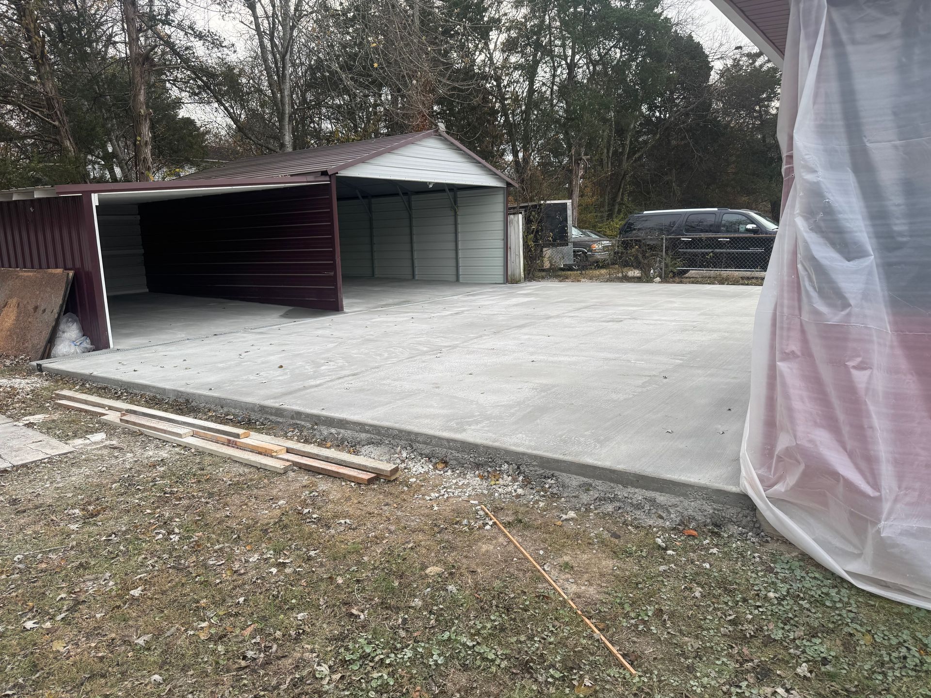 Concrete driveway with open carport, garage, and parked SUV beside a house in winter.