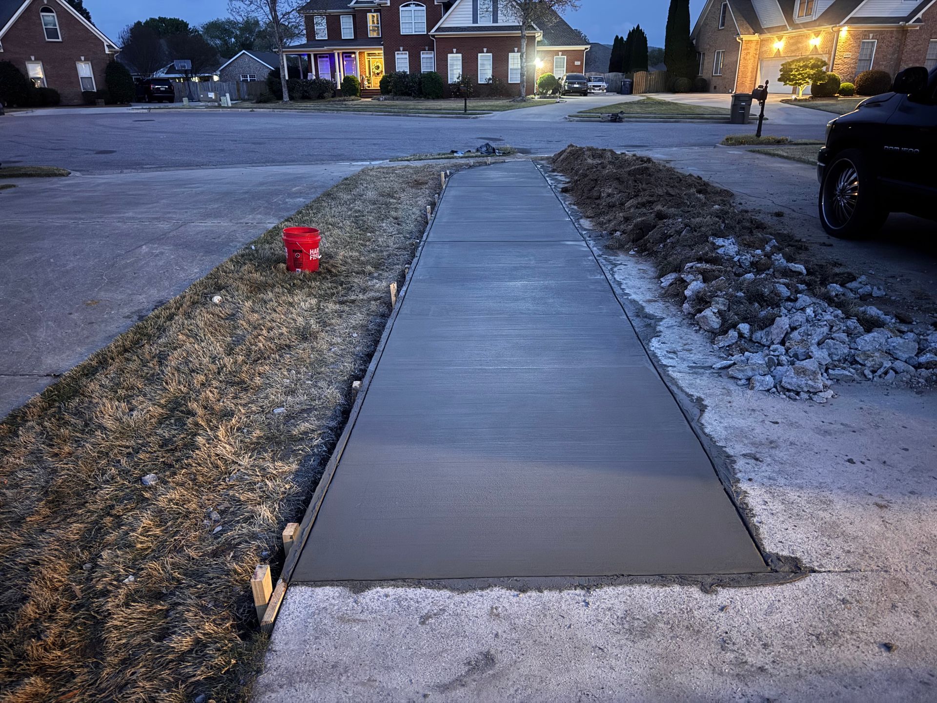 Concrete sidewalk under construction in a suburban neighborhood at dusk, with a red fire hydrant nearby