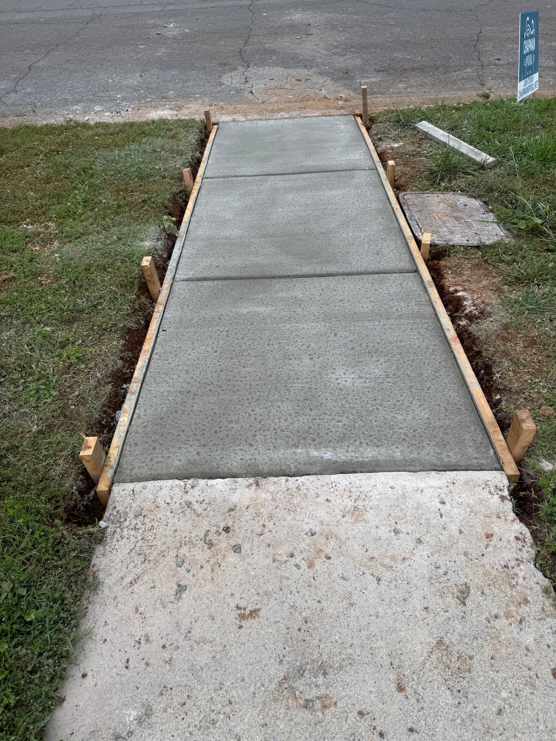 Concrete sidewalk ramp leading to a street, bordered by grass and small stones