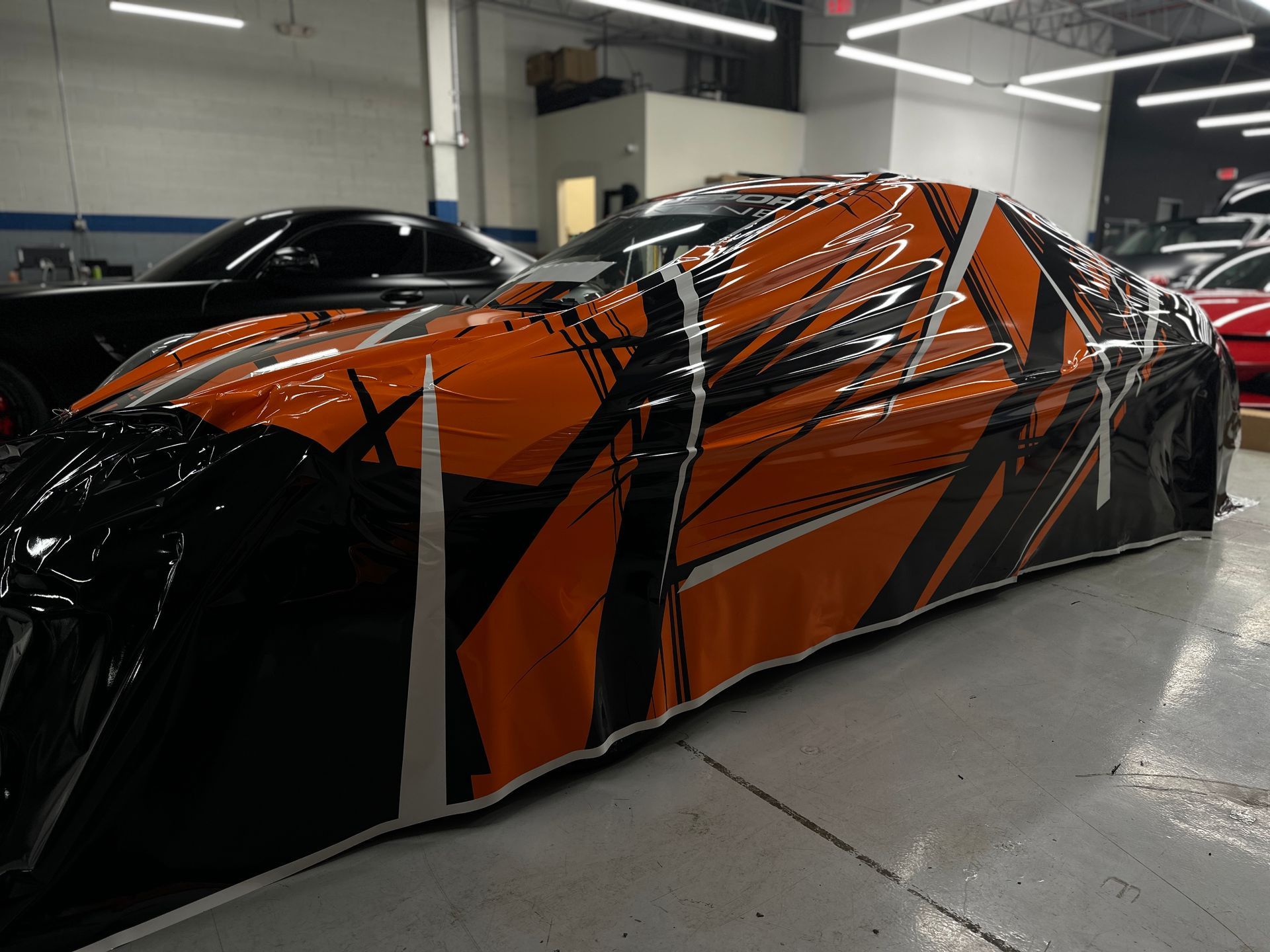 Car covered in orange and black graphic wrap in an auto shop.