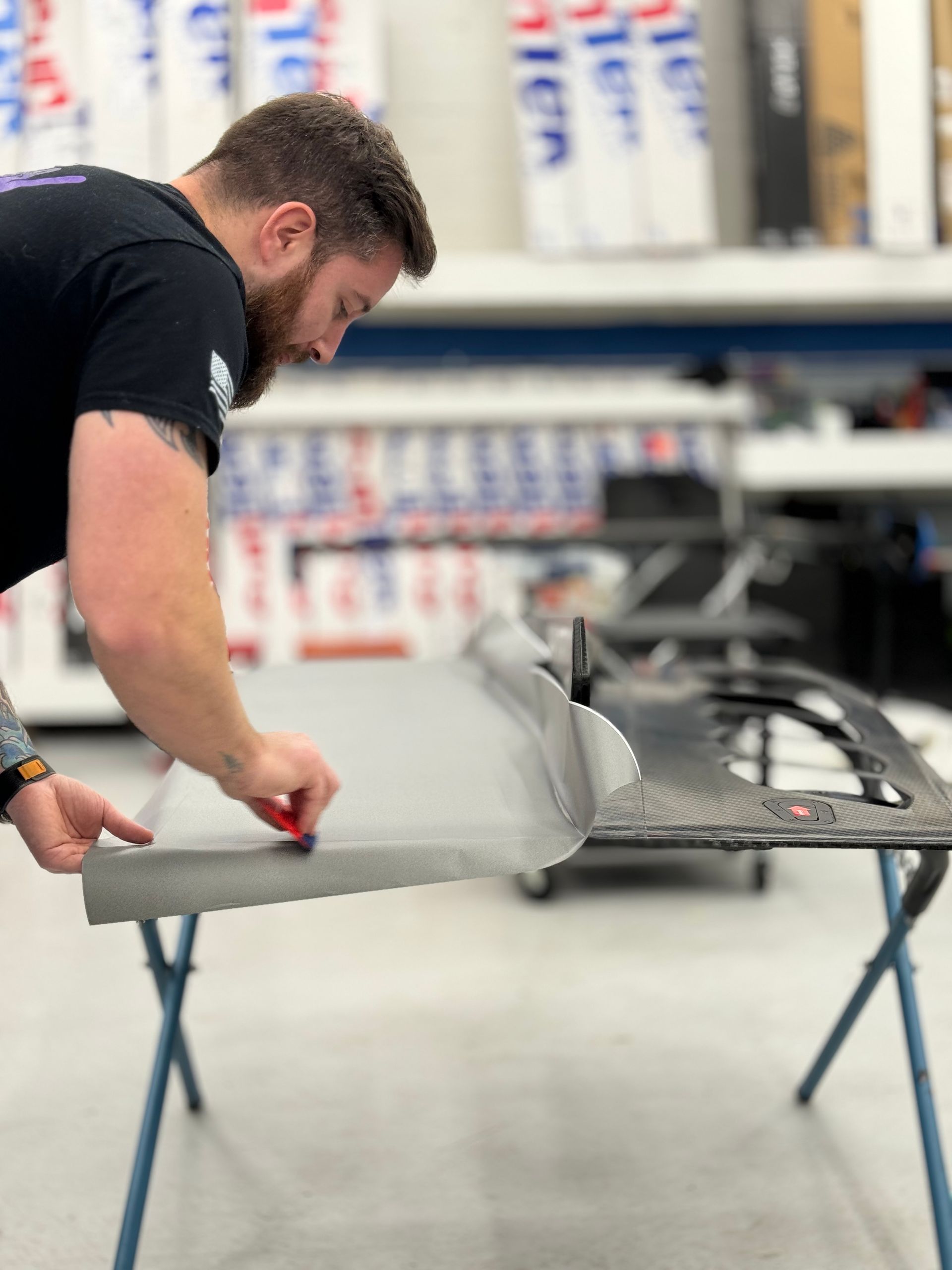 Man applying film to a car door, working at a table inside a shop.