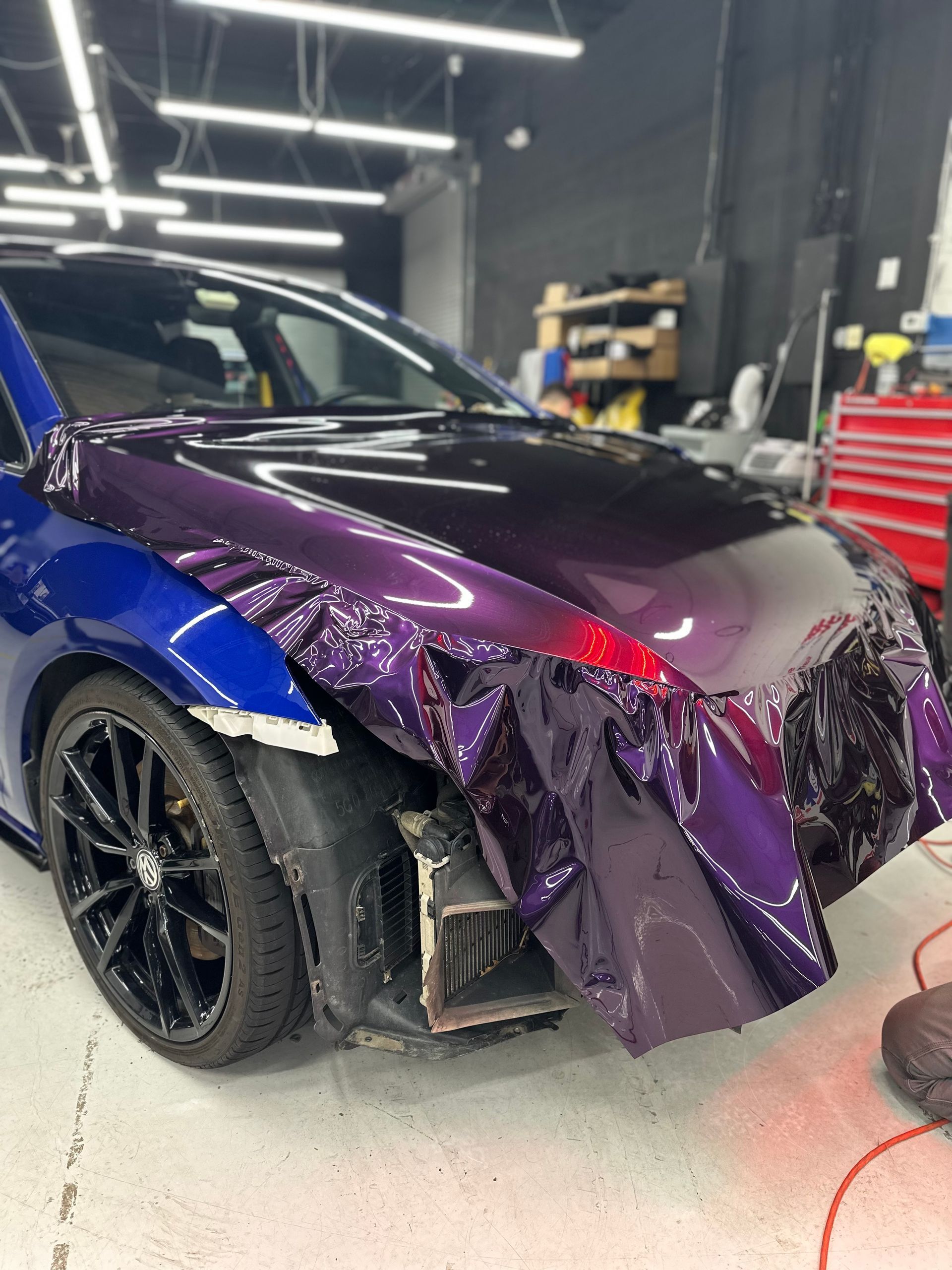 Car being wrapped in purple vinyl in a workshop. The blue side is contrasted by the purple hood and bumper wrap.
