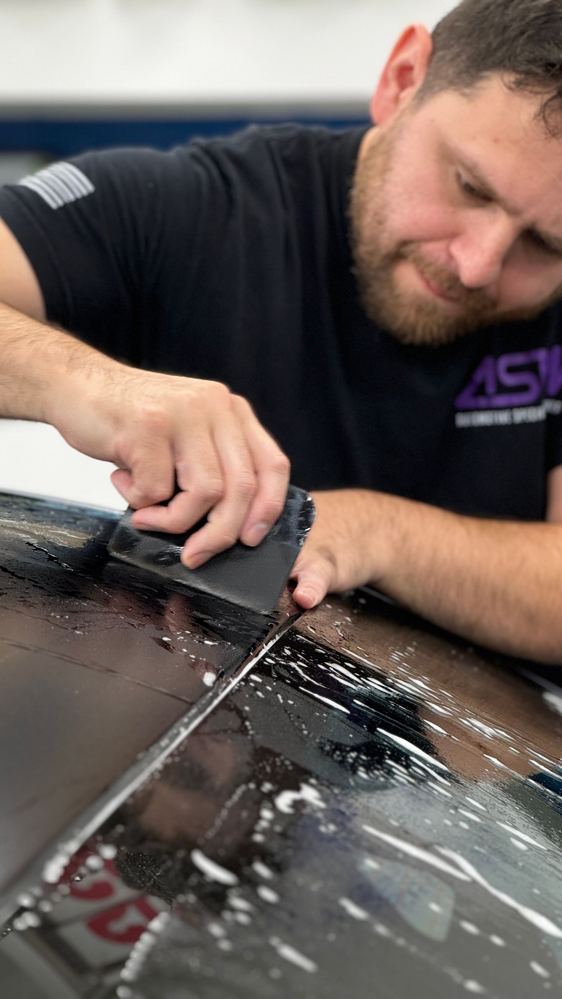 A man is cleaning the roof of a car with a sponge.