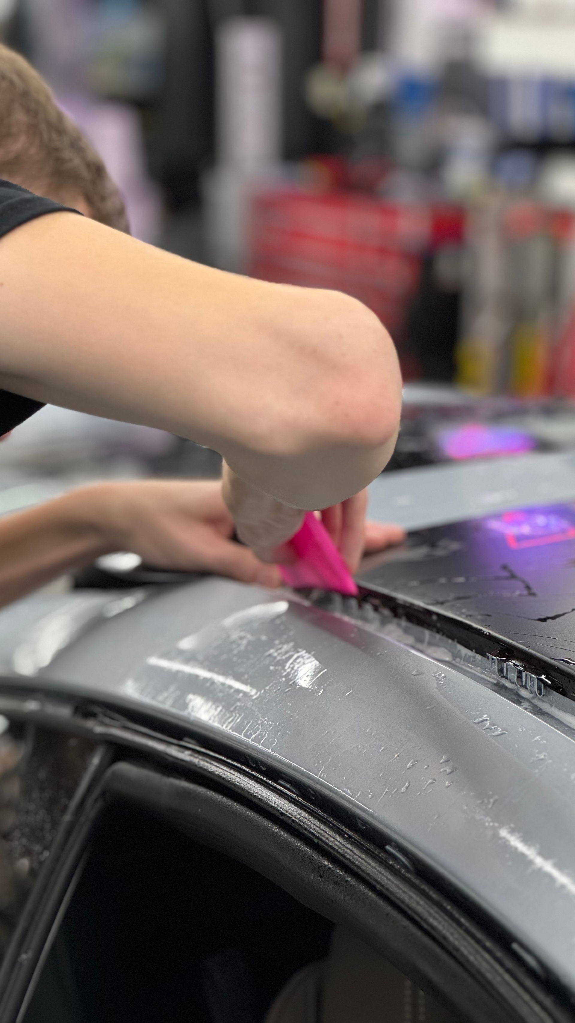 A person is applying a protective film to the roof of a car.
