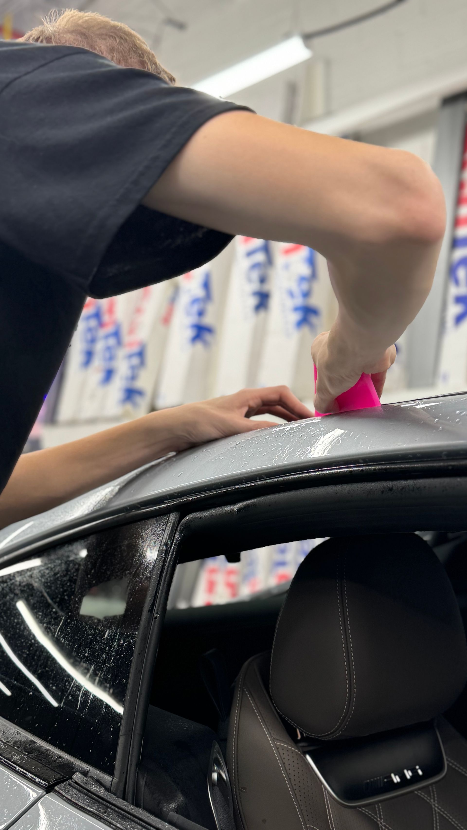 A man is applying a protective film to the roof of a car.
