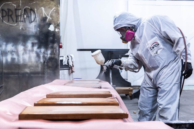 A man in a protective suit is spray painting wooden boards.